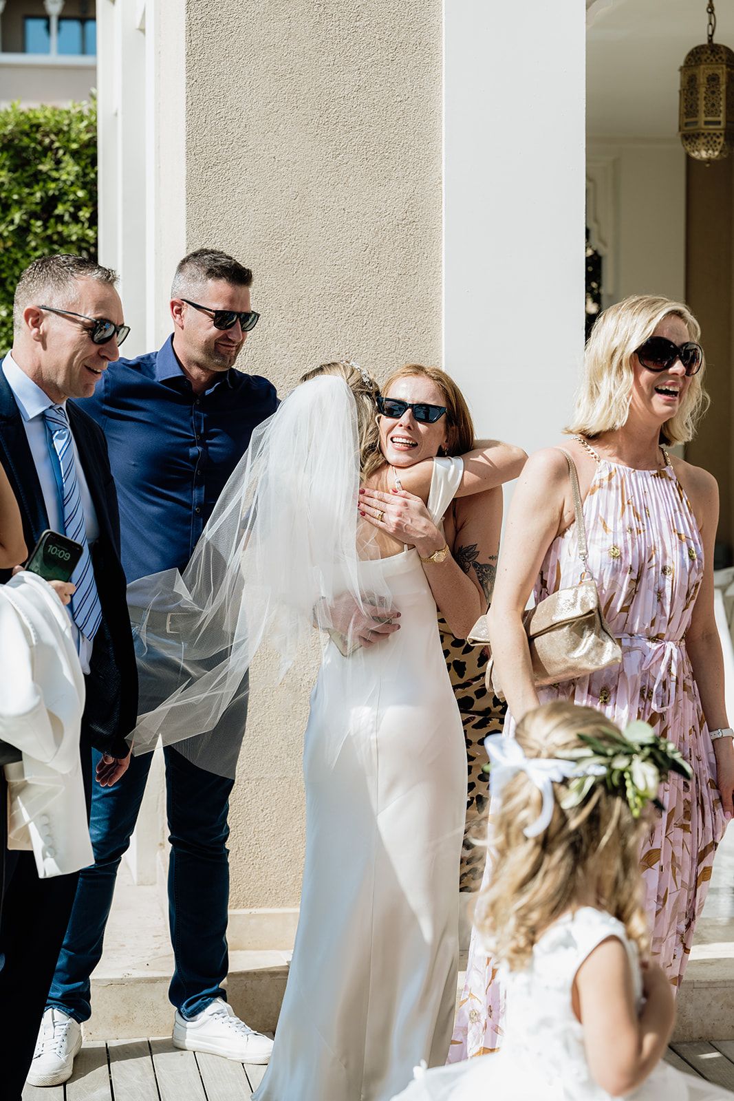 Wedding party celebrates with laughter and hugs on a bright porch with white columns.