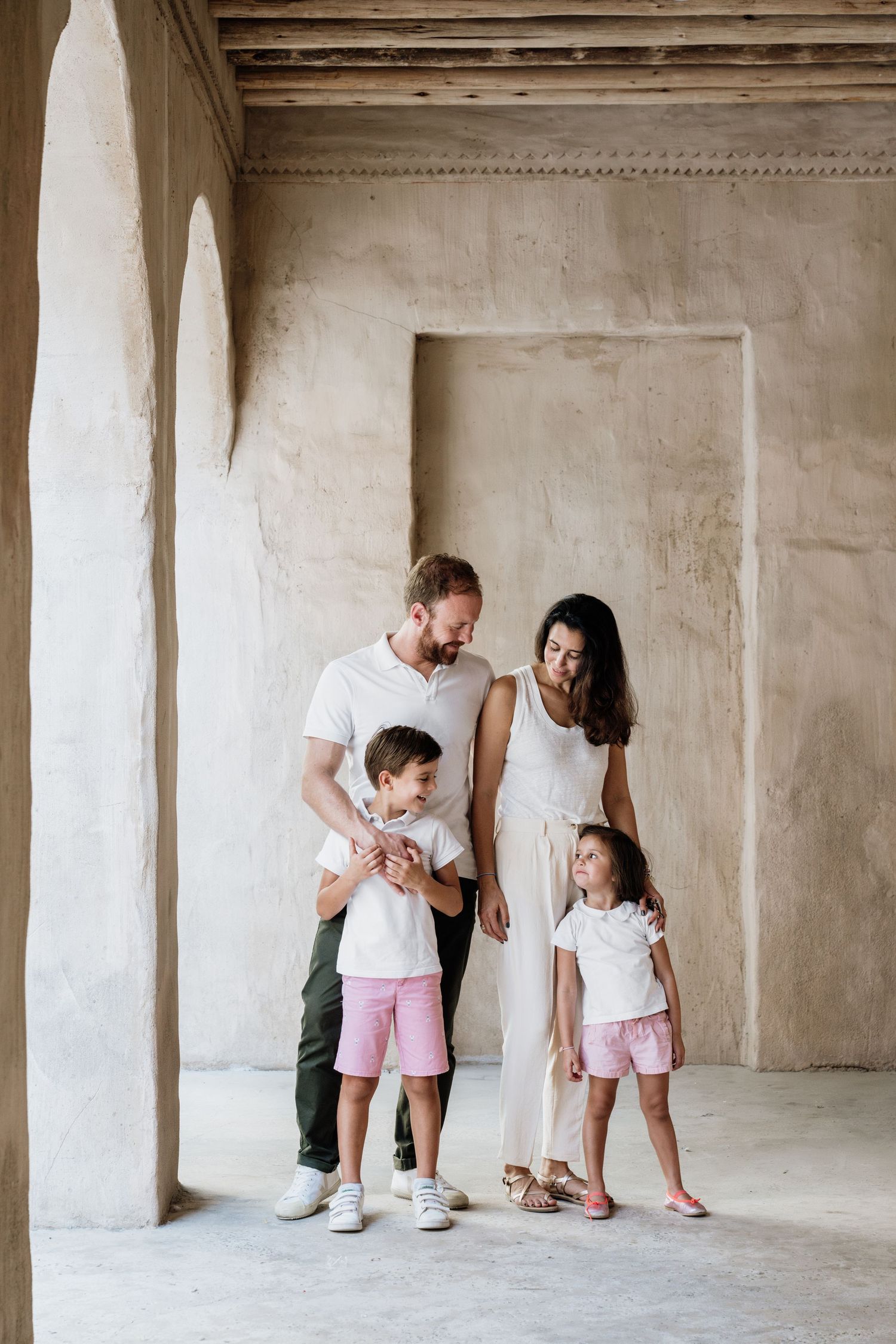 Family dressed in coordinating white outfits poses together in architectural space with columns.