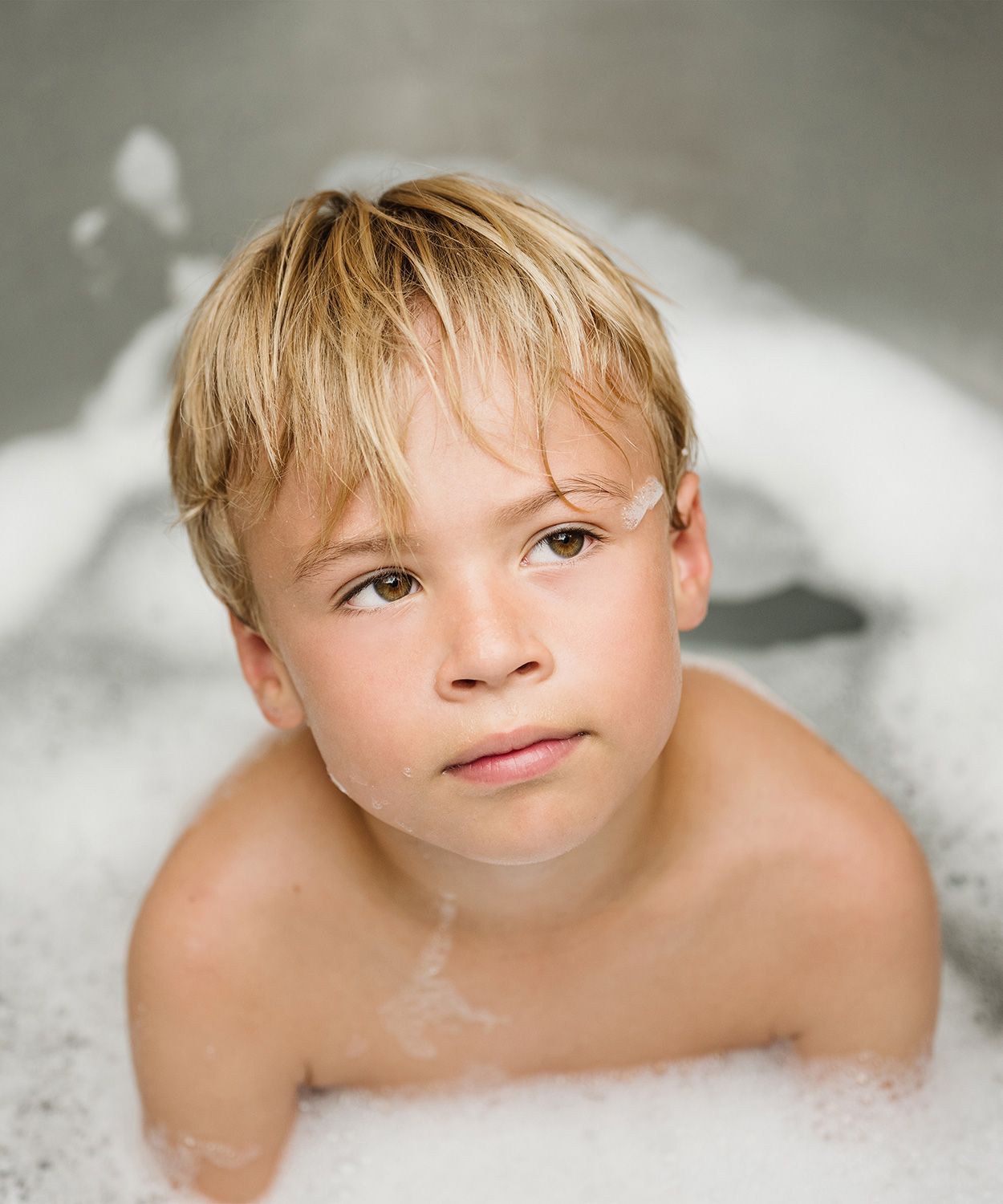A child plays in a bubble bath, creating a playful and whimsical series of portraits with soap bubbles.