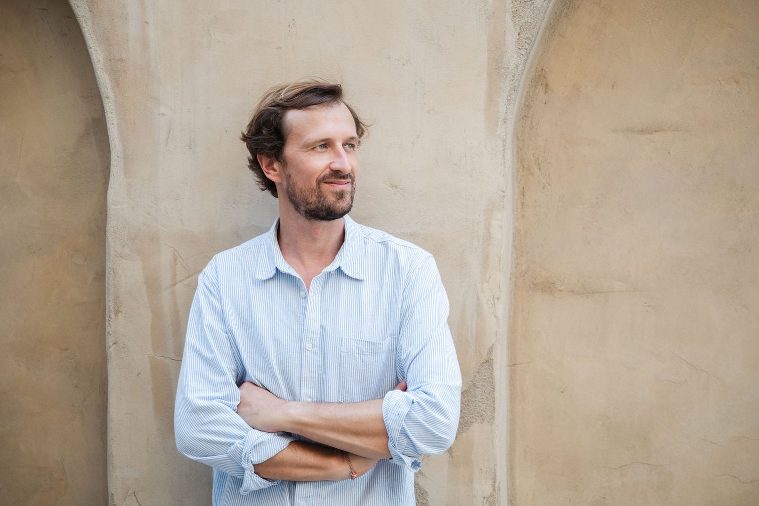 Man in light blue shirt posing against textured beige wall.