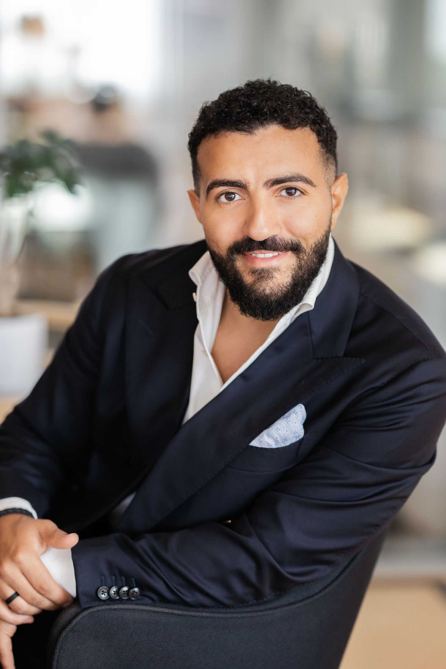 Professional headshots of person in dark suit smiling against office backdrop.