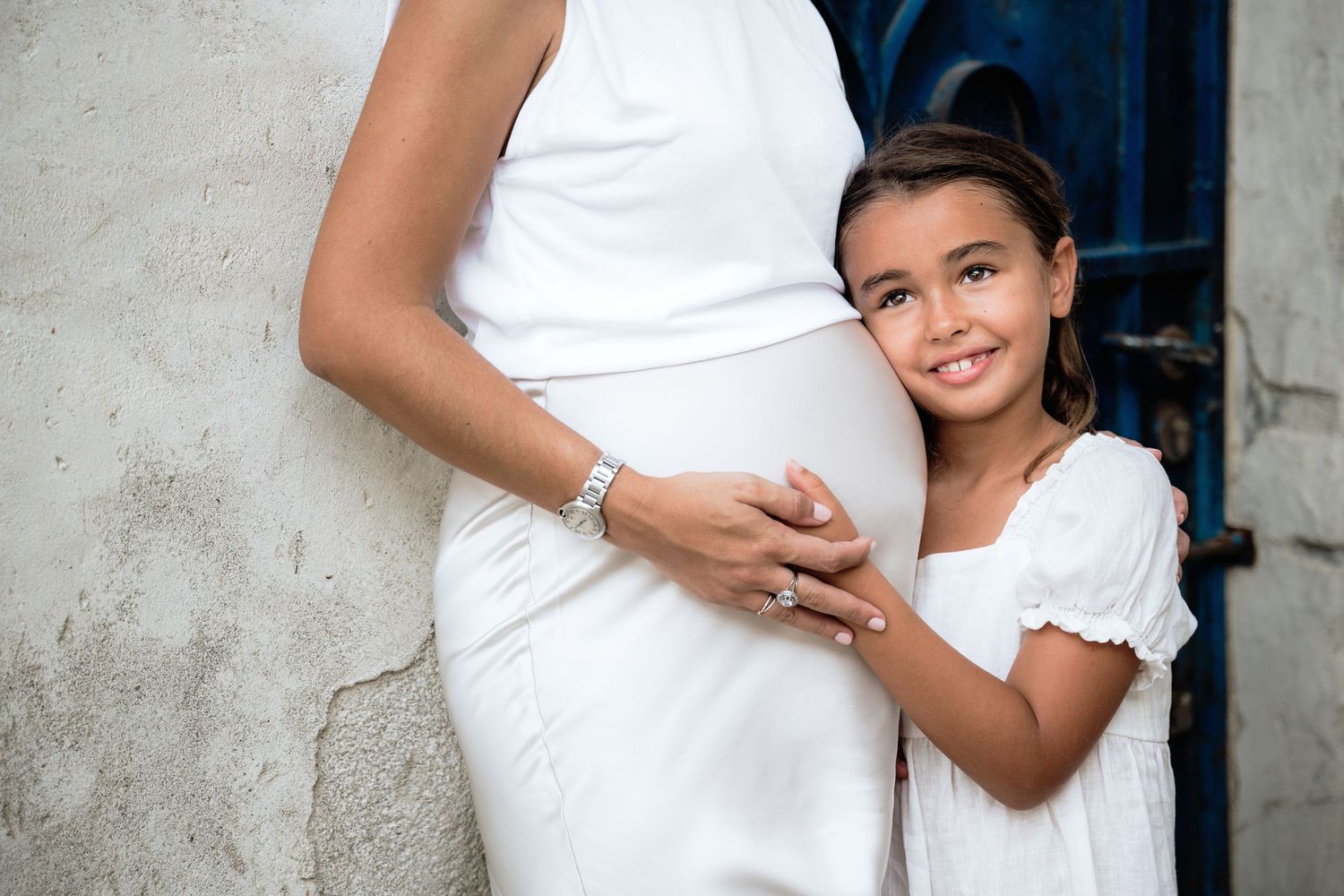 Maternity photos showing mother and child embracing against neutral wall.