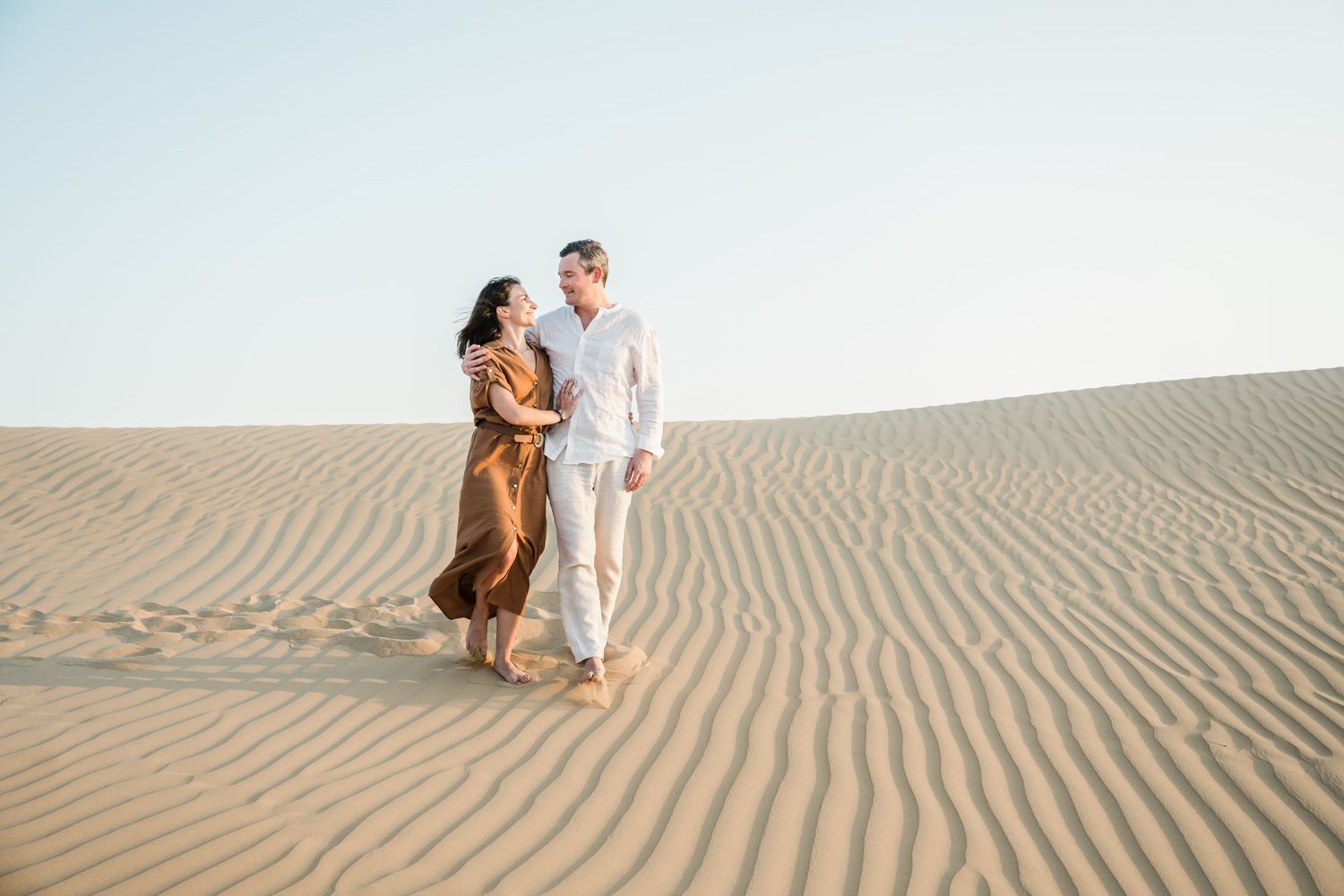 Couple walking and embracing on sandy desert dunes during a photoshoot.
