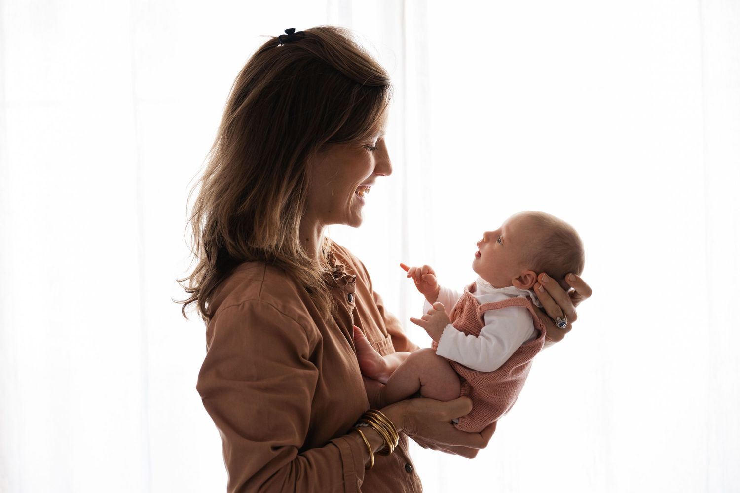 Silhouette of mother and baby against bright window, sharing tender moment.