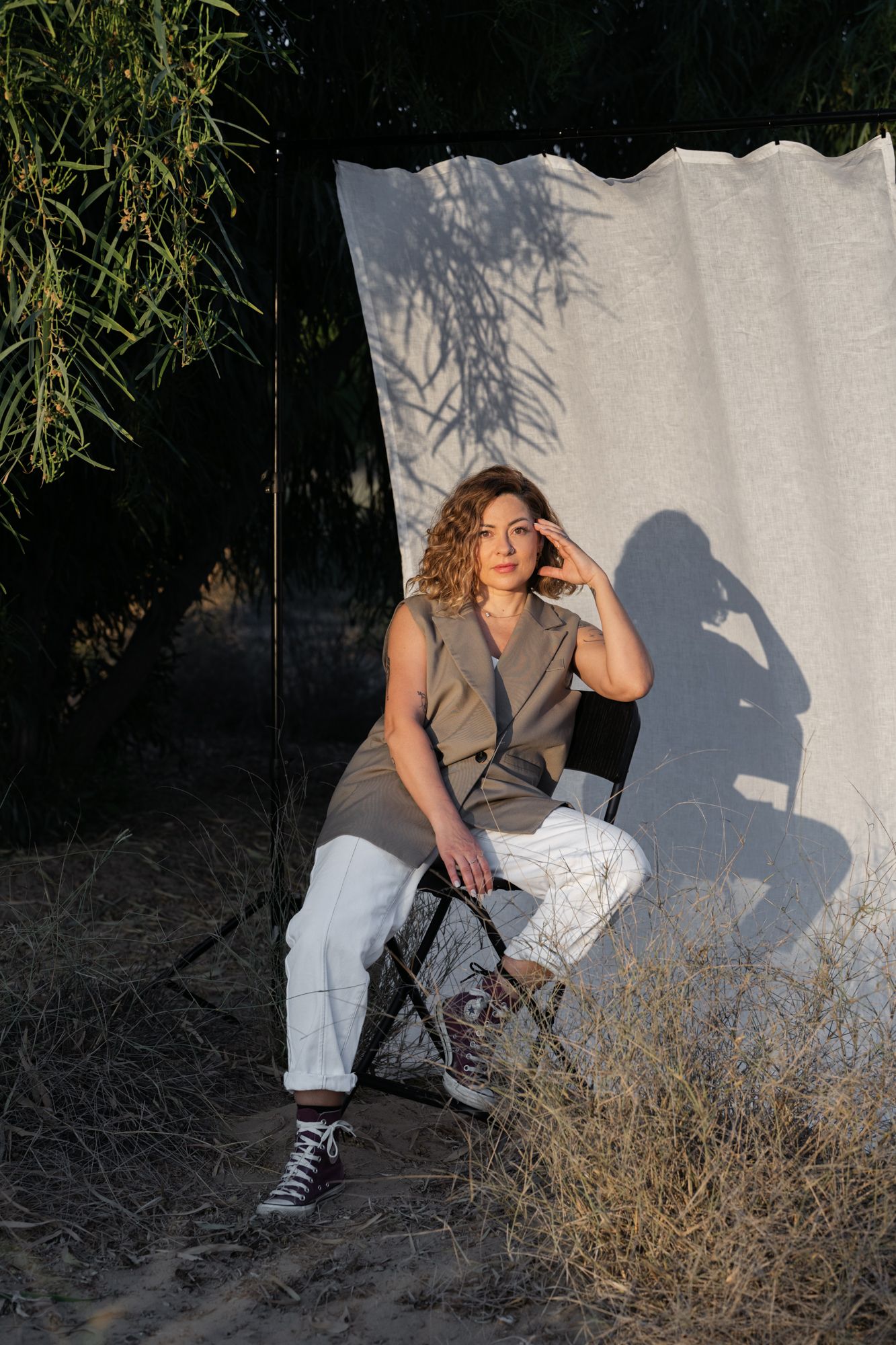 A woman in casual attire sits against a white backdrop outdoors, casting a dramatic shadow in natural sunlight.