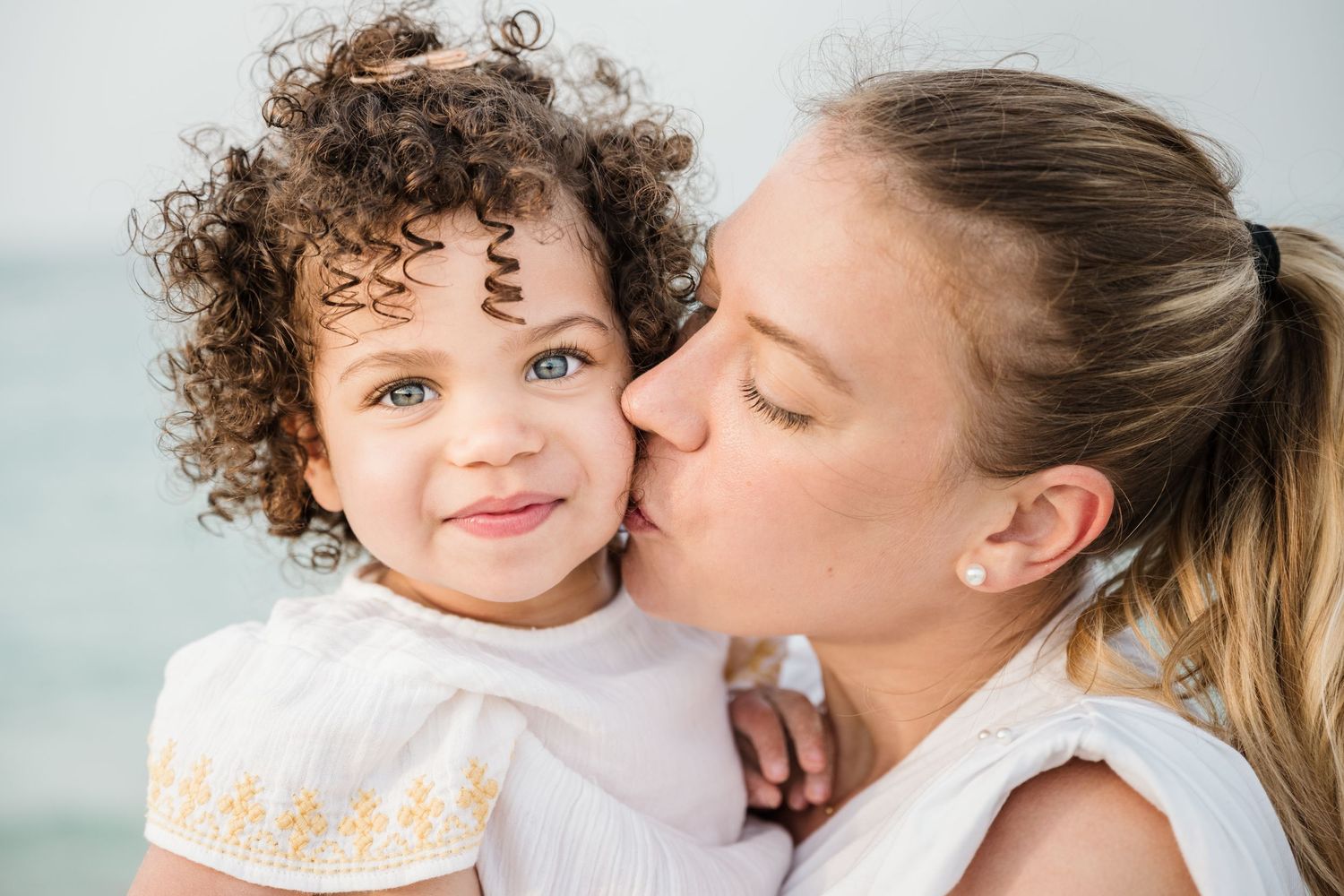 Mother and child share tender moment against light background.