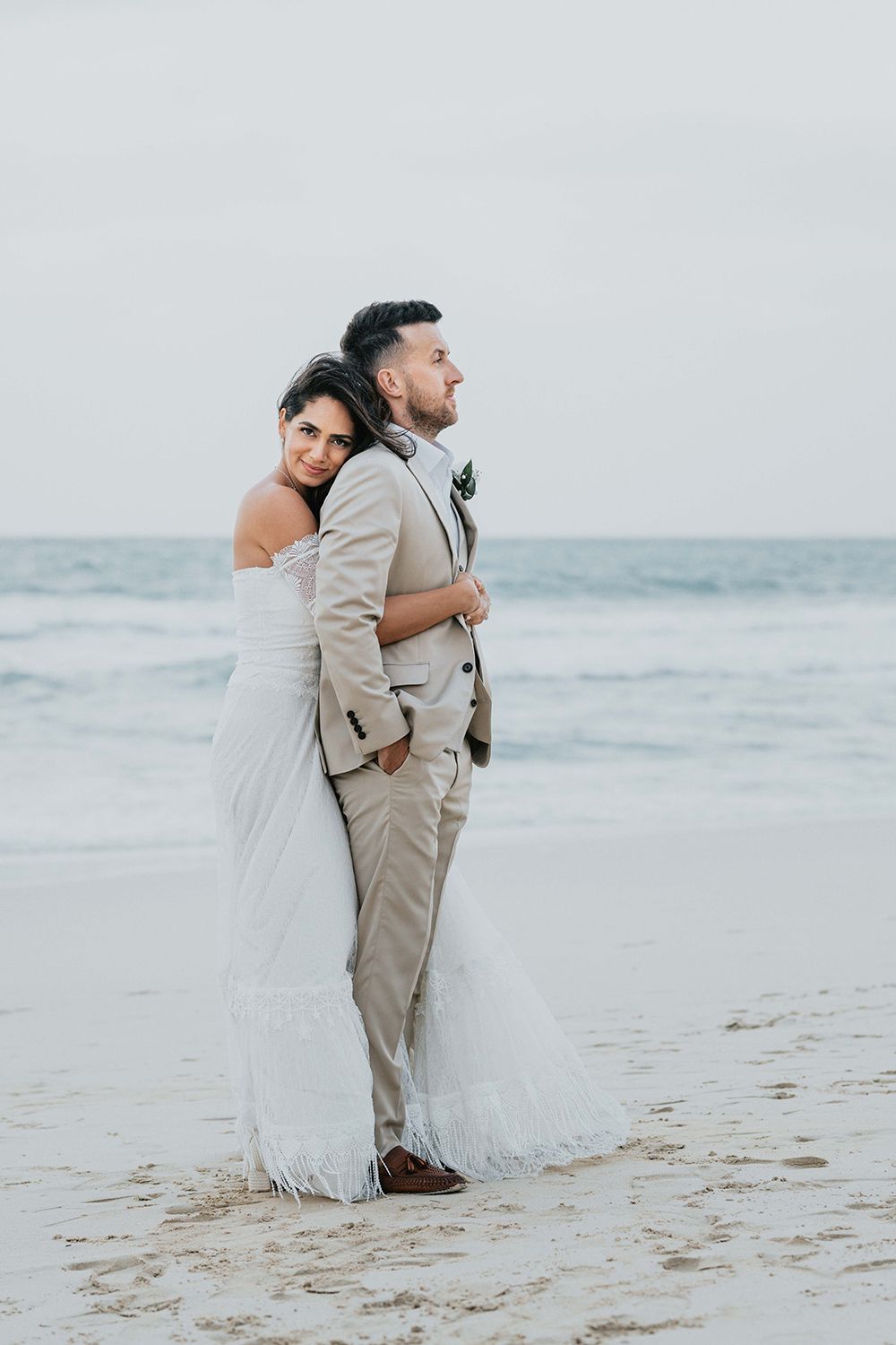 Artistic wedding photography on sandy beach with gentle waves in background.