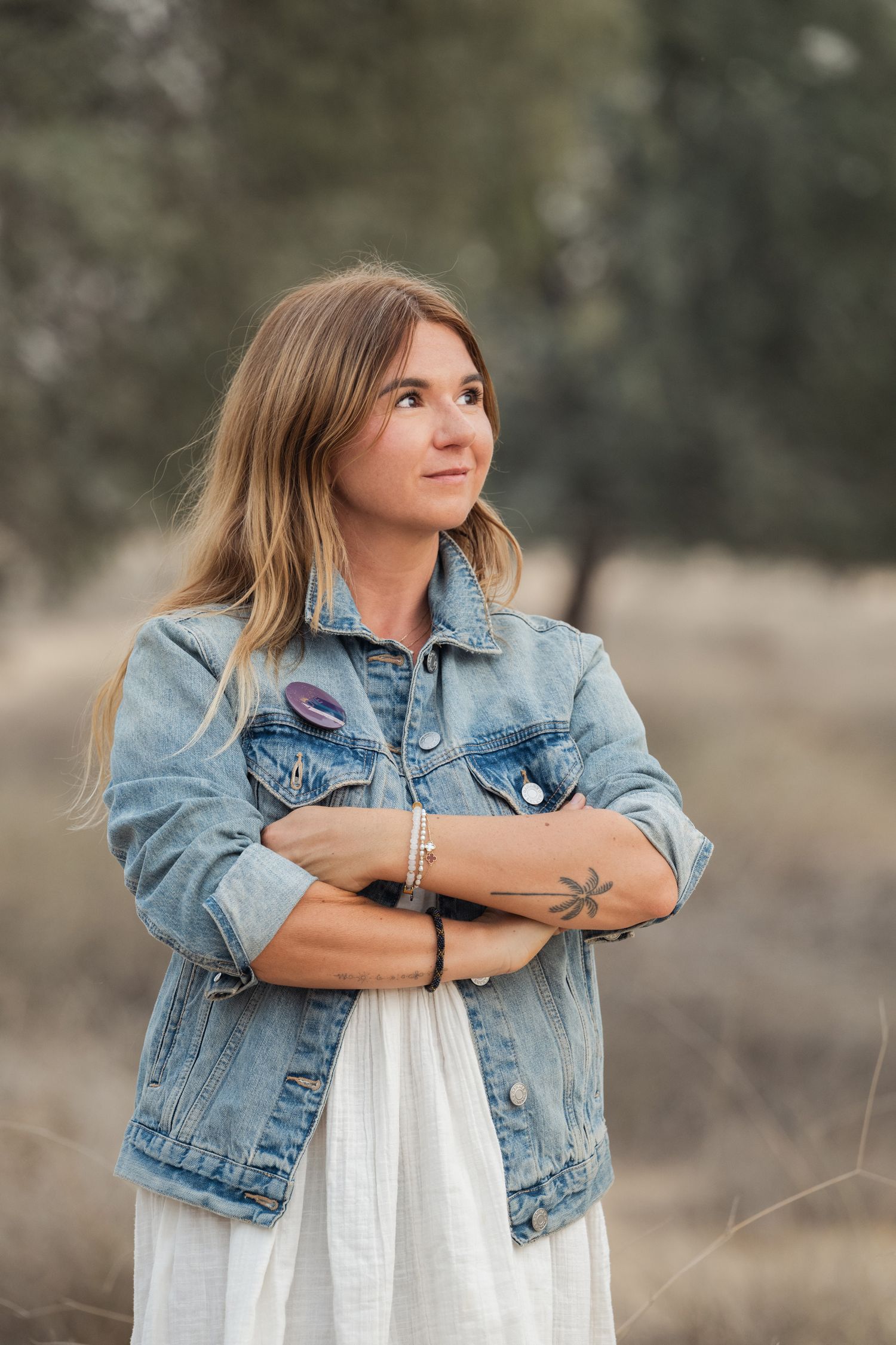 A dreamy outdoor portrait featuring a denim jacket and white dress against a soft blurred natural background.