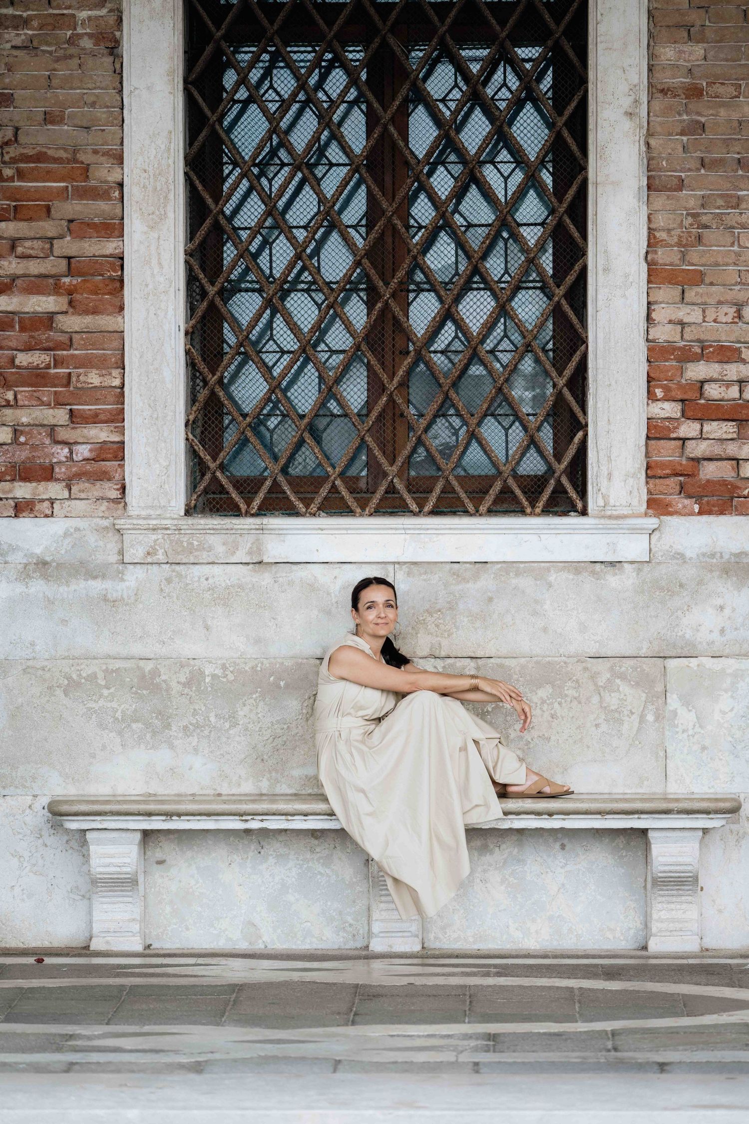 Cream-colored dress contrasts against historic Venetian architecture with brick walls and arched windows.