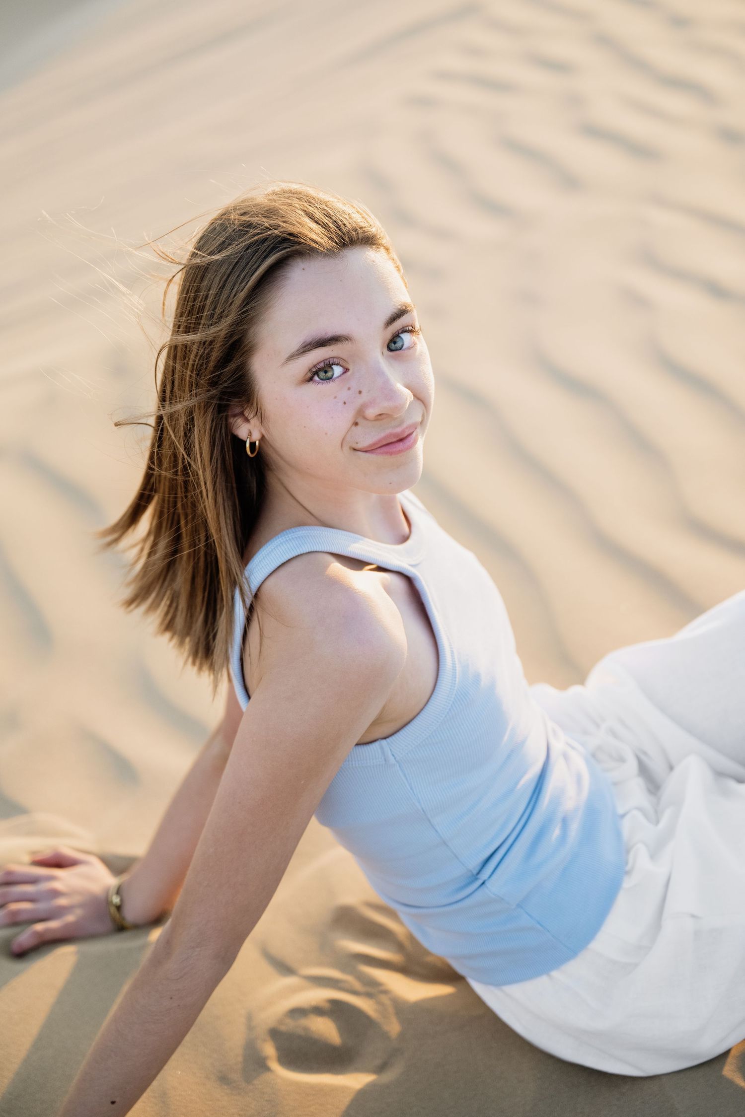 Person in white tank top posing on sandy dunes during golden hour photoshoot.