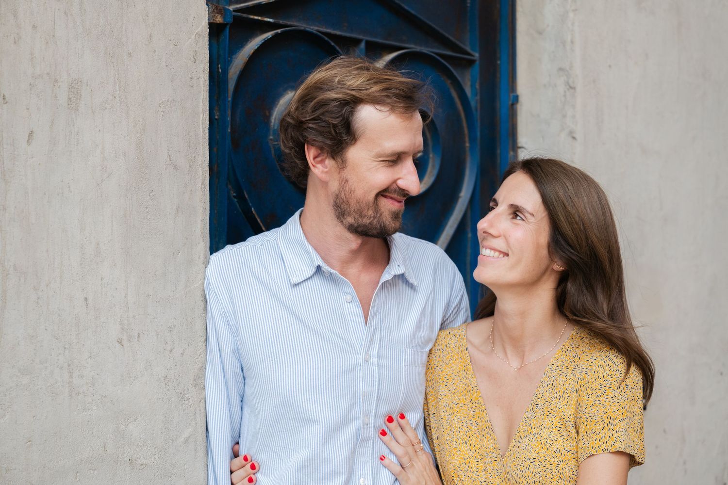 Couple in blue shirt and yellow dress sharing tender moments against textured wall.