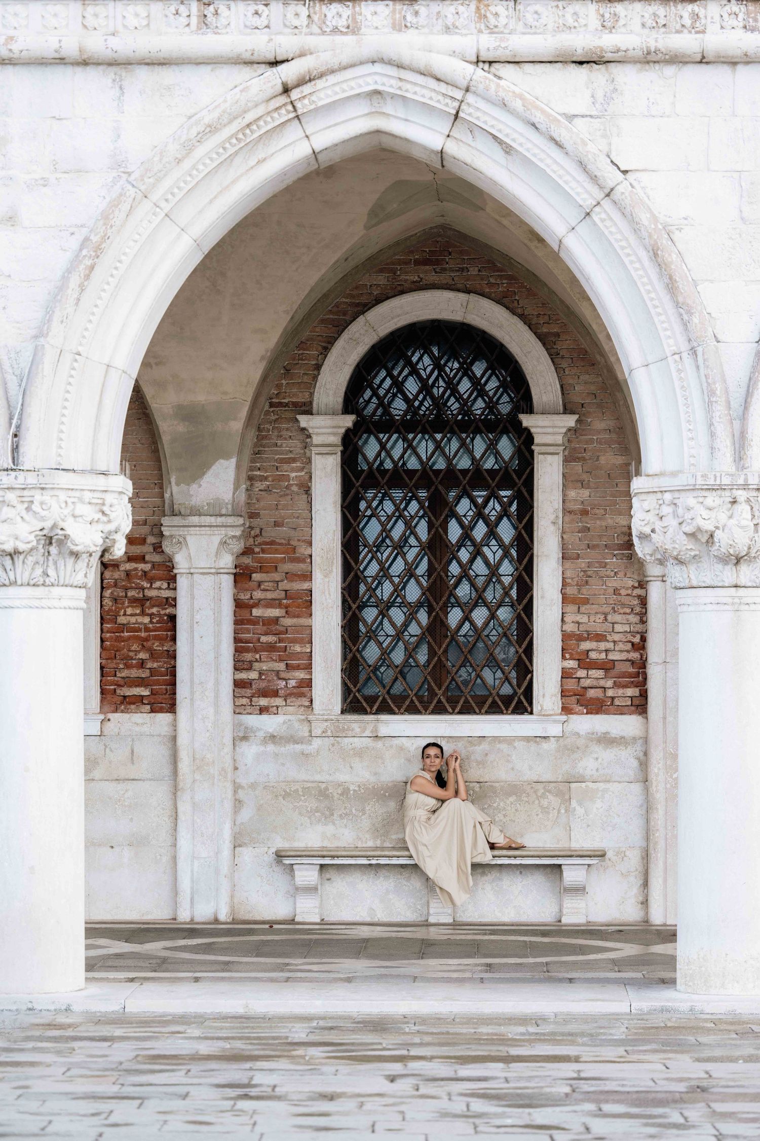 Historic Venetian architecture featuring white stone arches, brick walls, and ornate windows along a covered walkway.