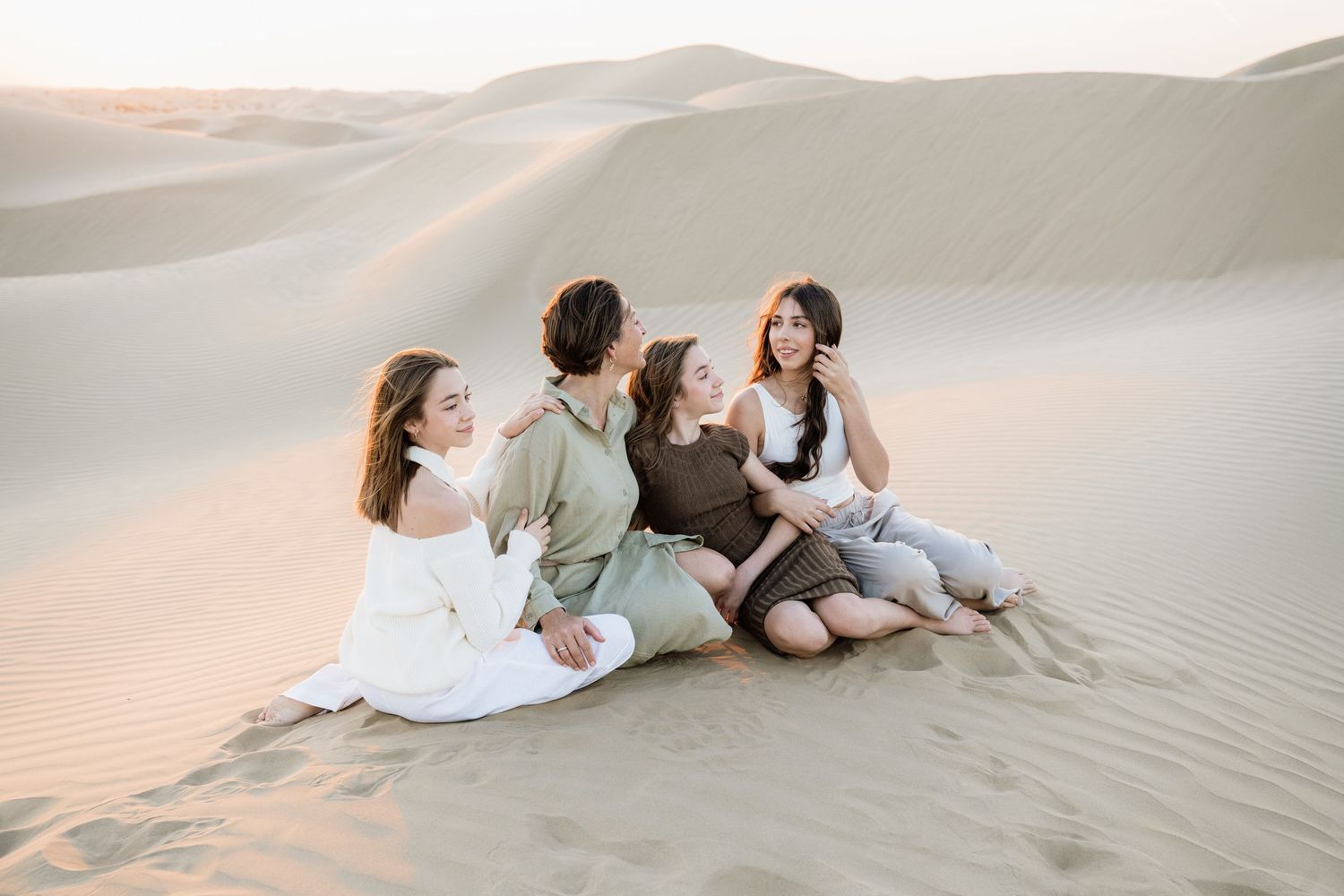 Friends lounging on sand dunes while enjoying desert sunset together.