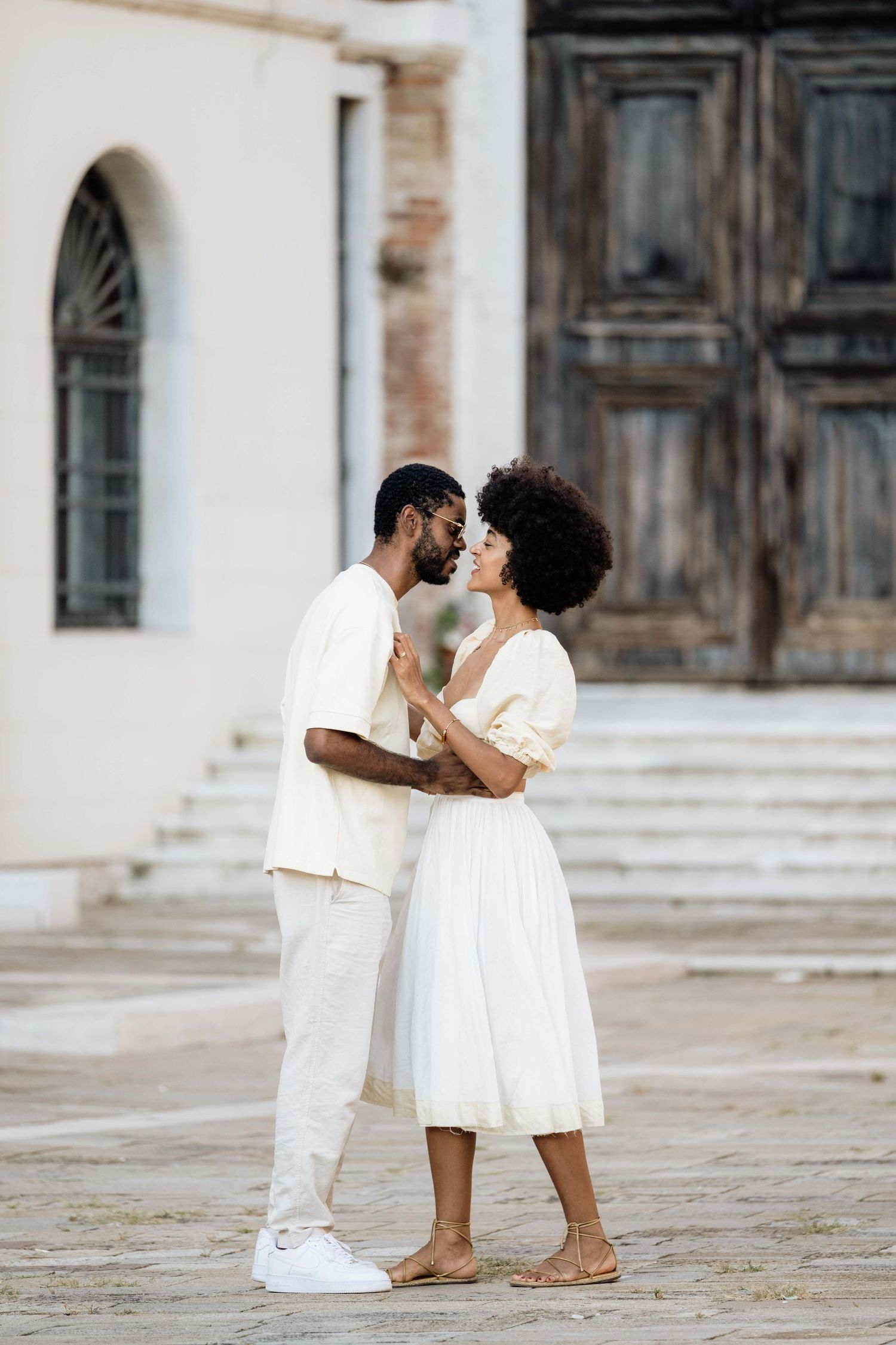 A romantic moment between a couple dressed in white against historic architecture.