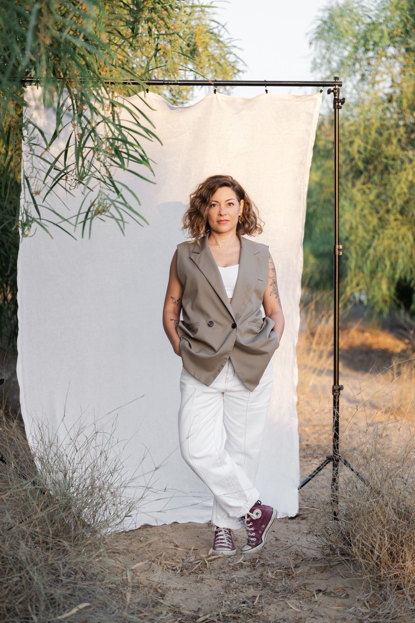 A lifestyle photo series showing a woman in a beige vest and white pants against a white backdrop outdoors in a fashion style