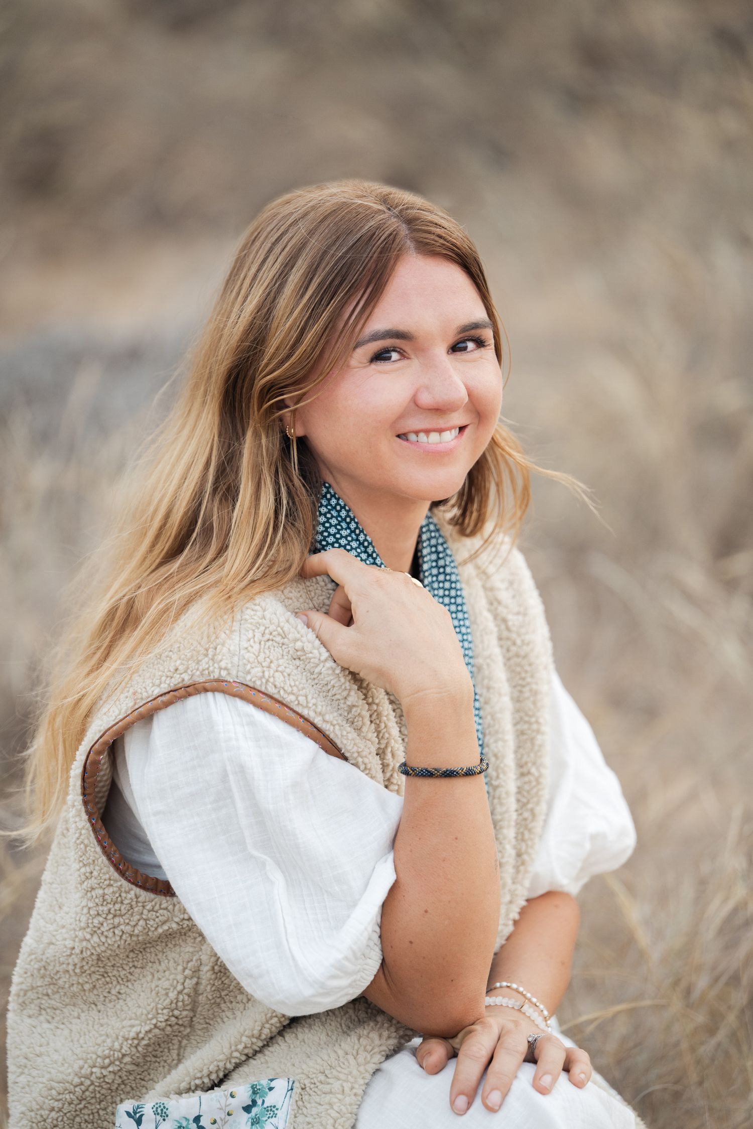 A person wearing a white sweater and polka dot scarf poses outdoors in a field with natural lighting and warm tones.