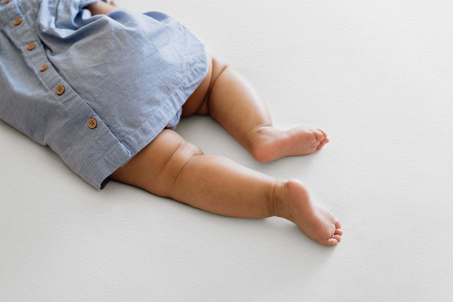 Close-up of tiny baby feet and blue dress details against white background.
