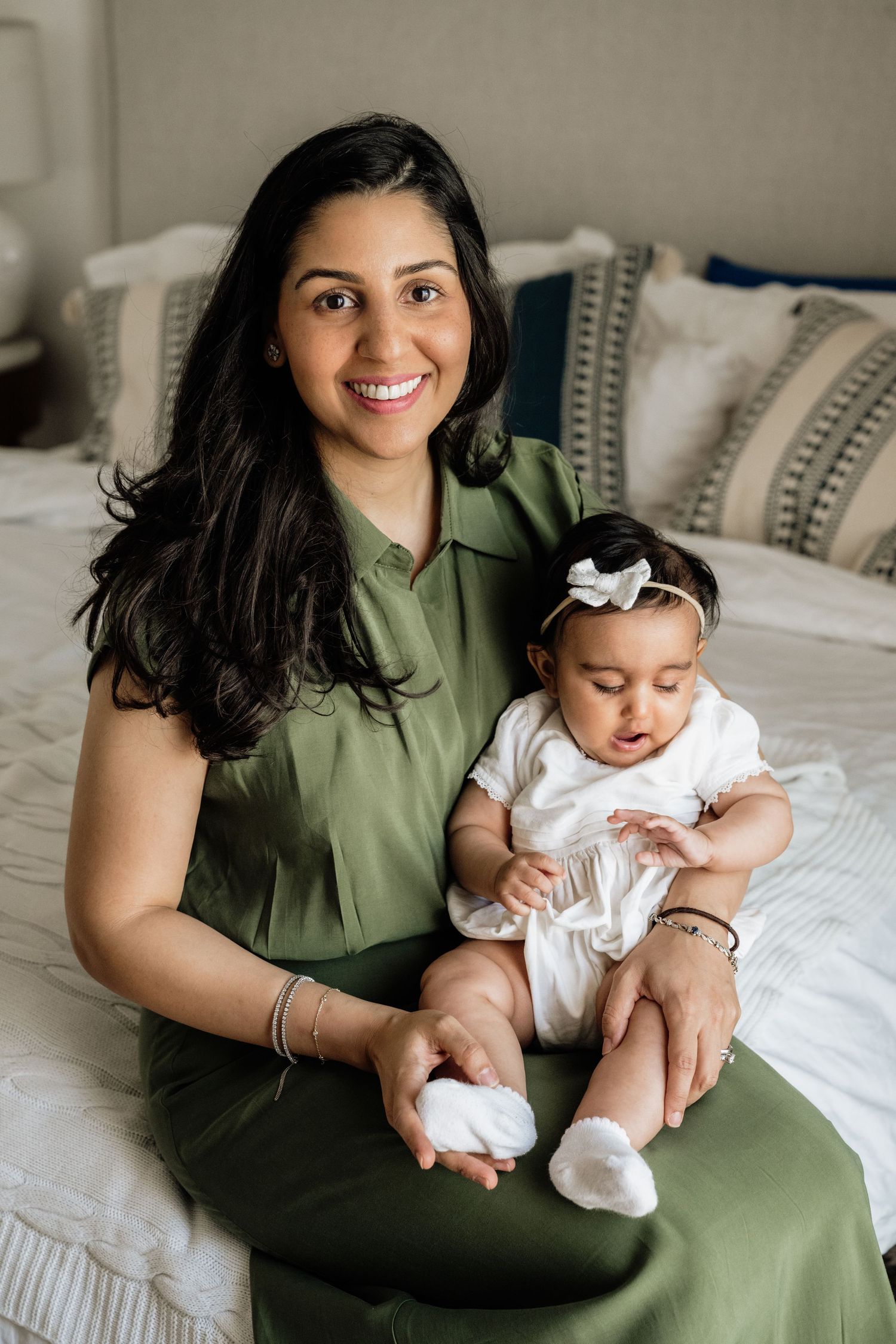 Sweet candid moments between parent in green dress and baby in white outfit on bed.