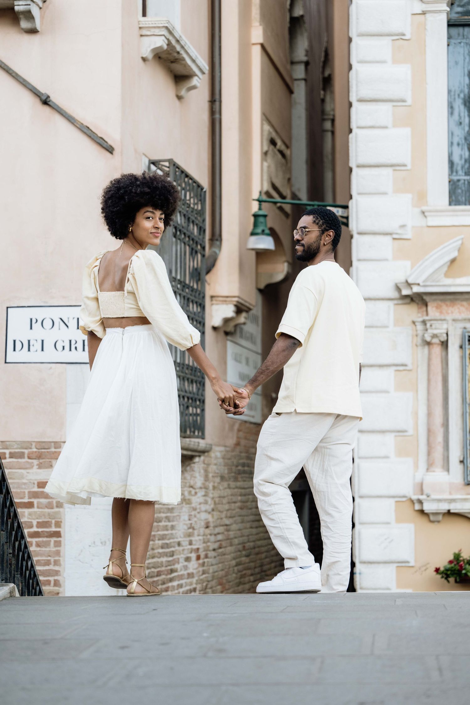 Couple in all-white outfits sharing romantic moments against a brick building exterior.