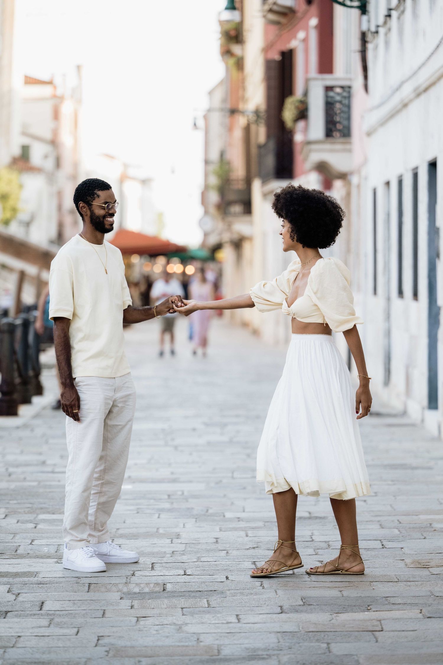 A couple in white clothing dances and plays on an empty European street.