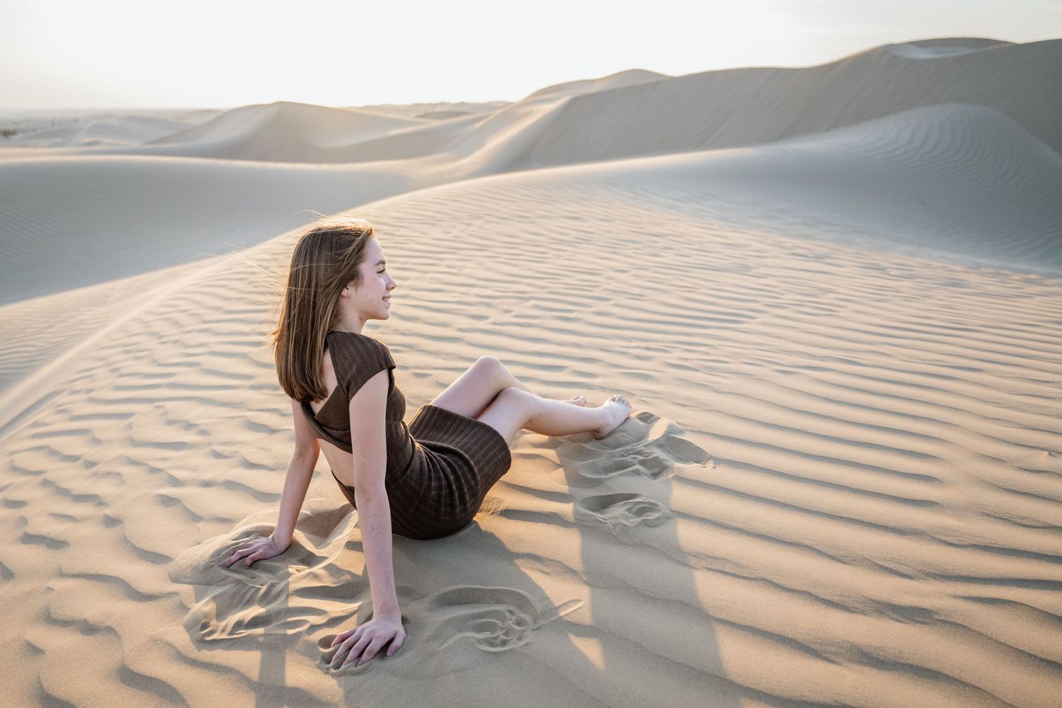 Person lying on rippled sand dunes during sunset creating long shadows.