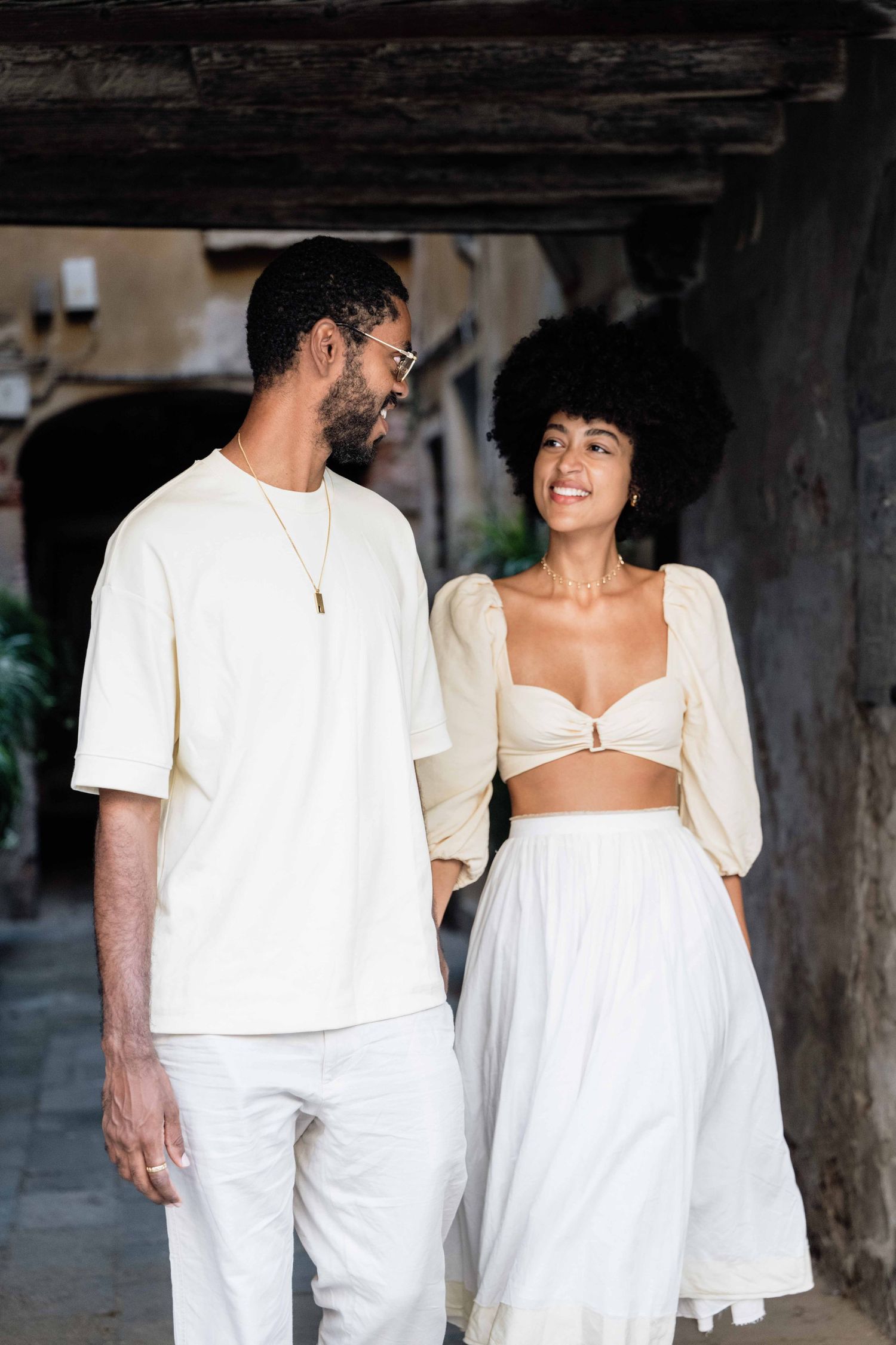 Stylish couple in white clothing sharing intimate moments in rustic setting.