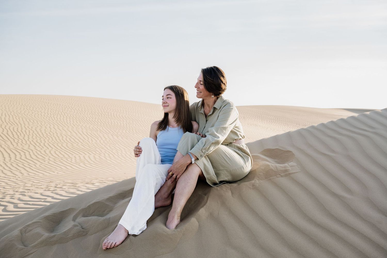 People sitting casually on desert sand dunes during sunset photoshoot.