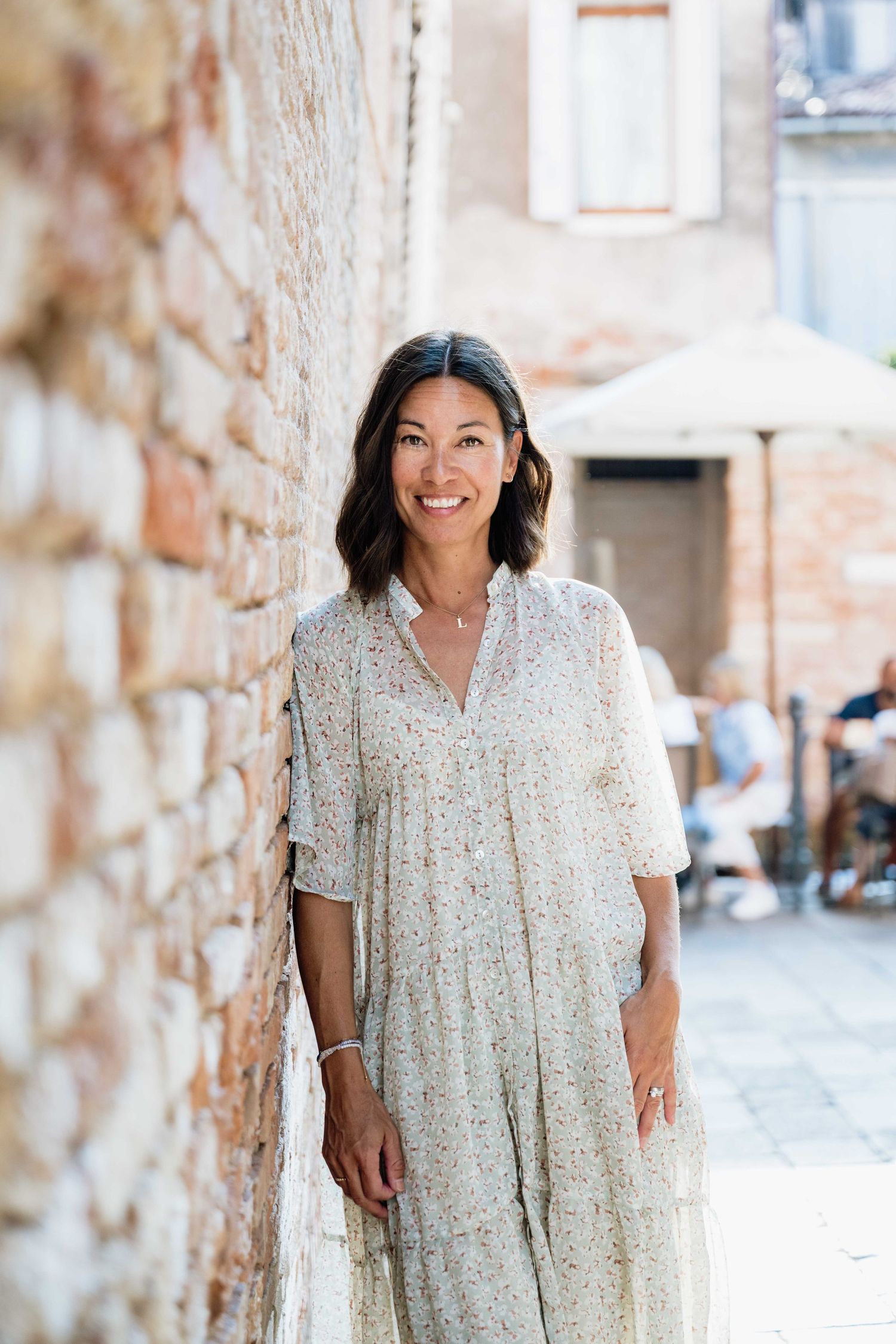 Person in light floral dress poses cheerfully against textured stone wall.