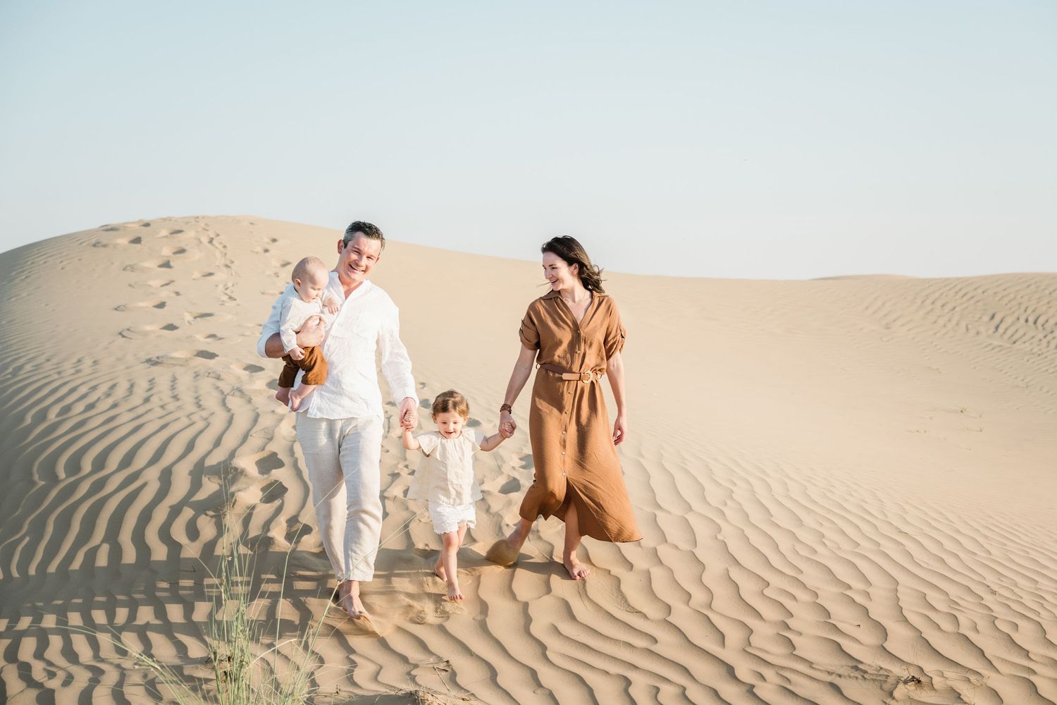 A group walks together across rippling sand dunes during a desert photoshoot at golden hour.
