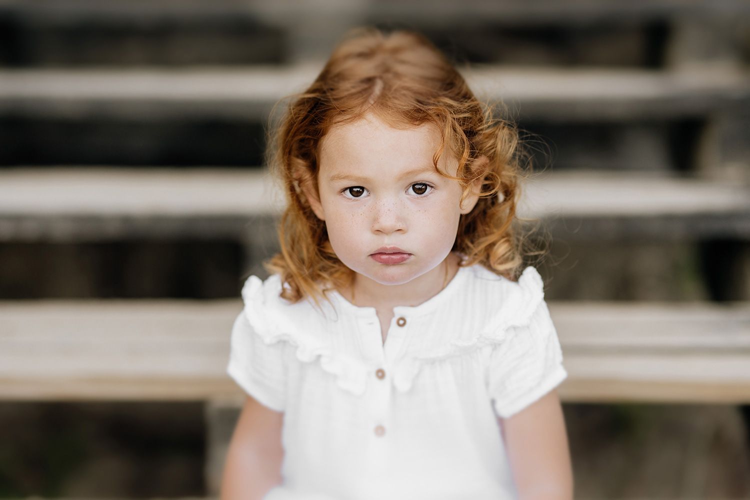 A young child in a white dress poses for a series of portraits against a dark background.