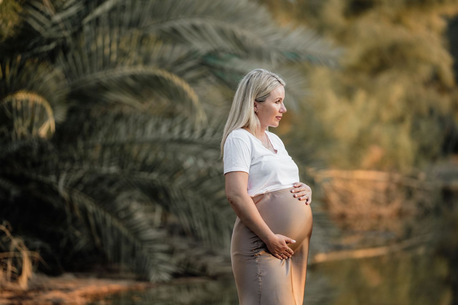 Maternity photo session in golden sunlight with palm trees in background.