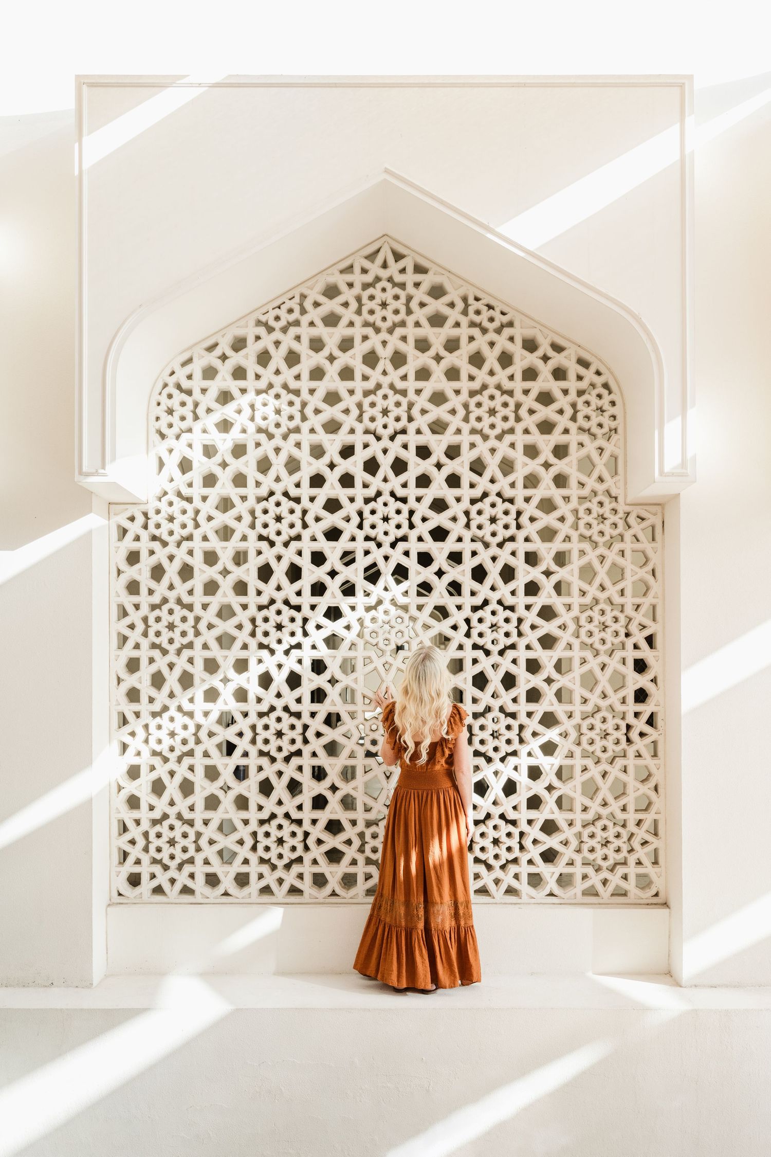 Ornate geometric Islamic lattice window with sunlight casting shadows and orange dress display.