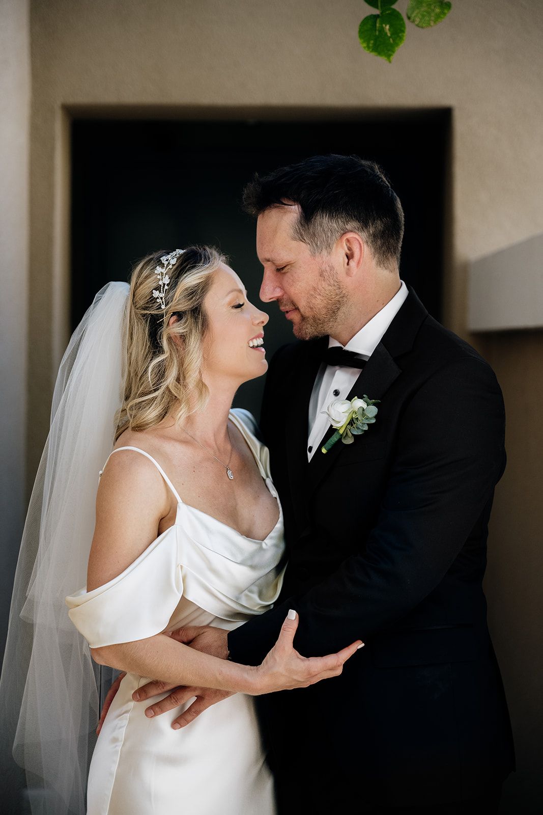 Bride in white gown and groom in tuxedo share intimate dance poses near window.