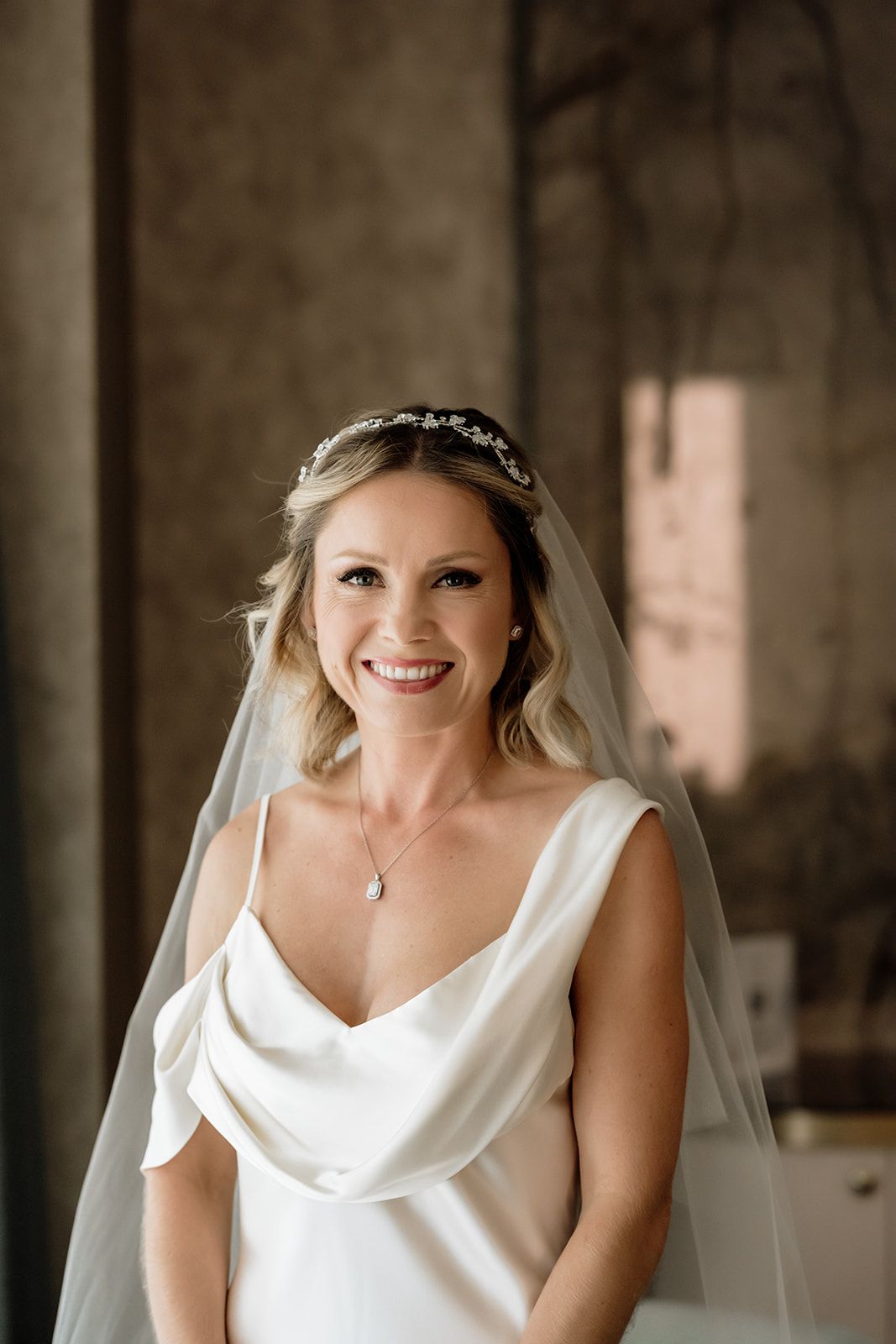Bride wearing elegant white cowl neck dress and veil smiles radiantly.