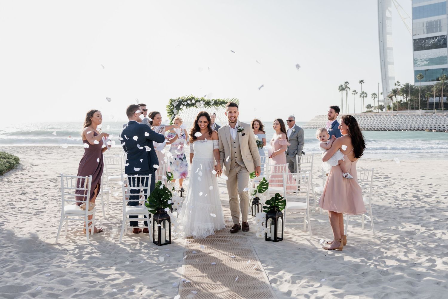 Intimate beachfront wedding ceremony with guests seated in white chairs as waves crash in the background.