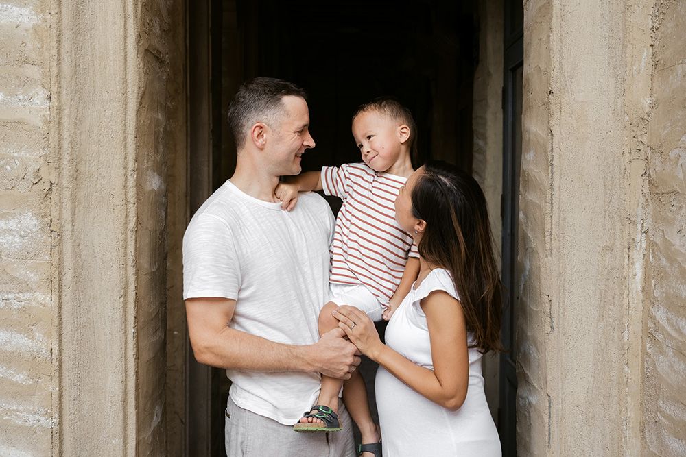 A couple in white outfits shares romantic moments against stone columns in an engagement or wedding photoshoot.