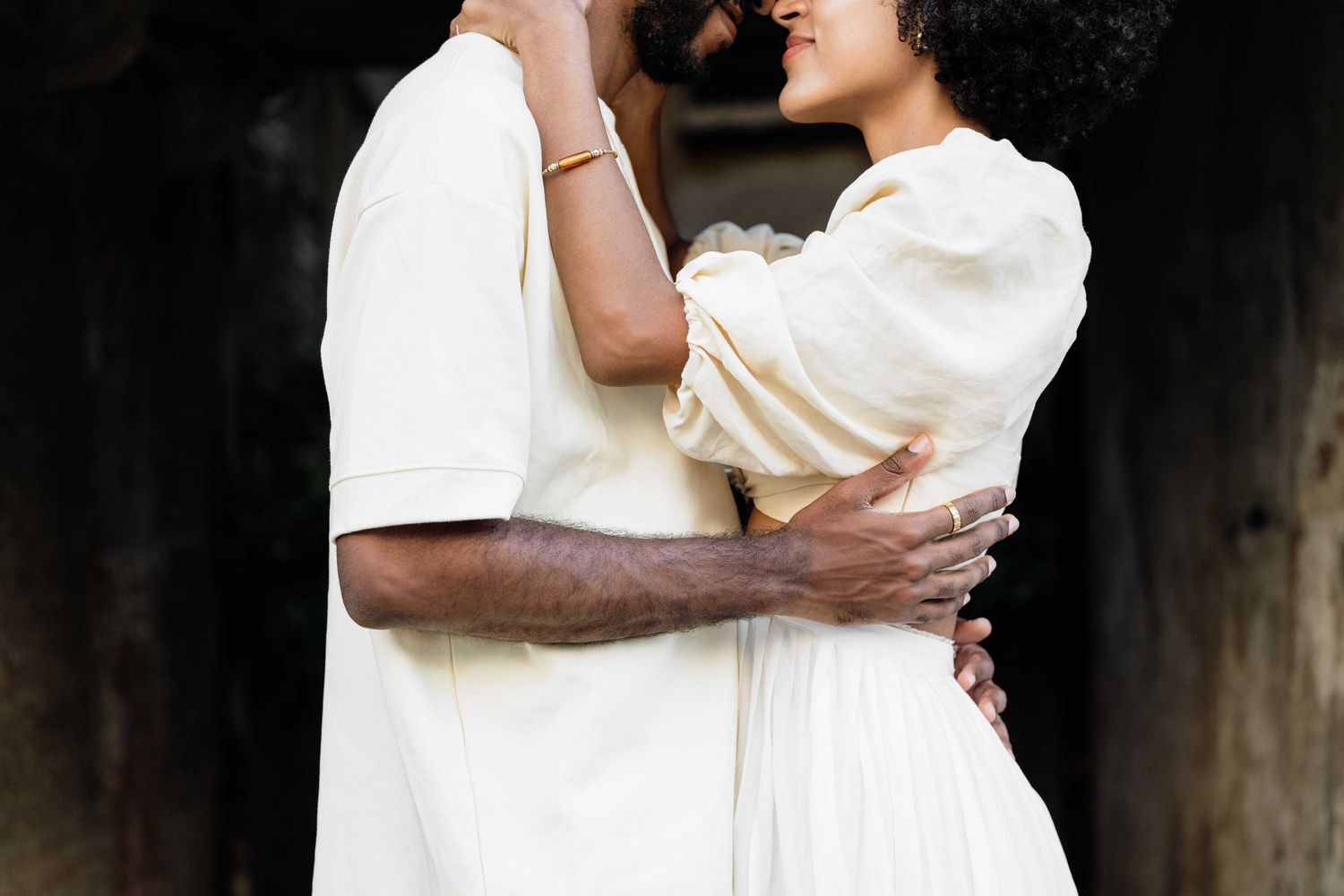 Loving couple in white attire embracing in atmospheric dark setting.