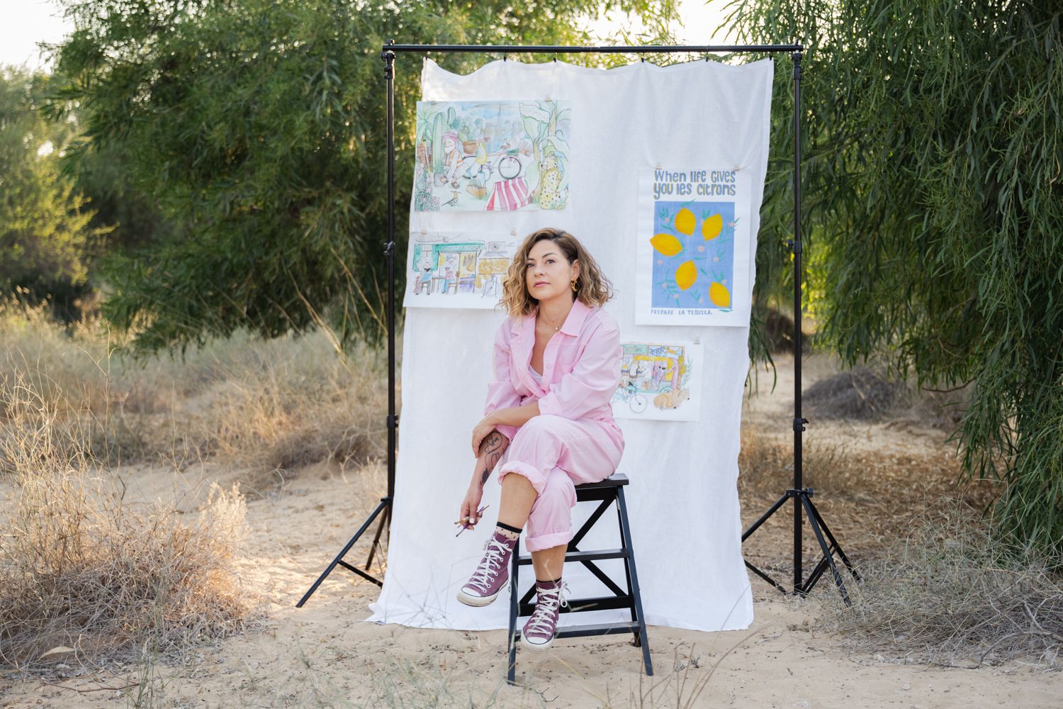 Professional photoshoot setup in nature with a white linen backdrop and black stool against trees.