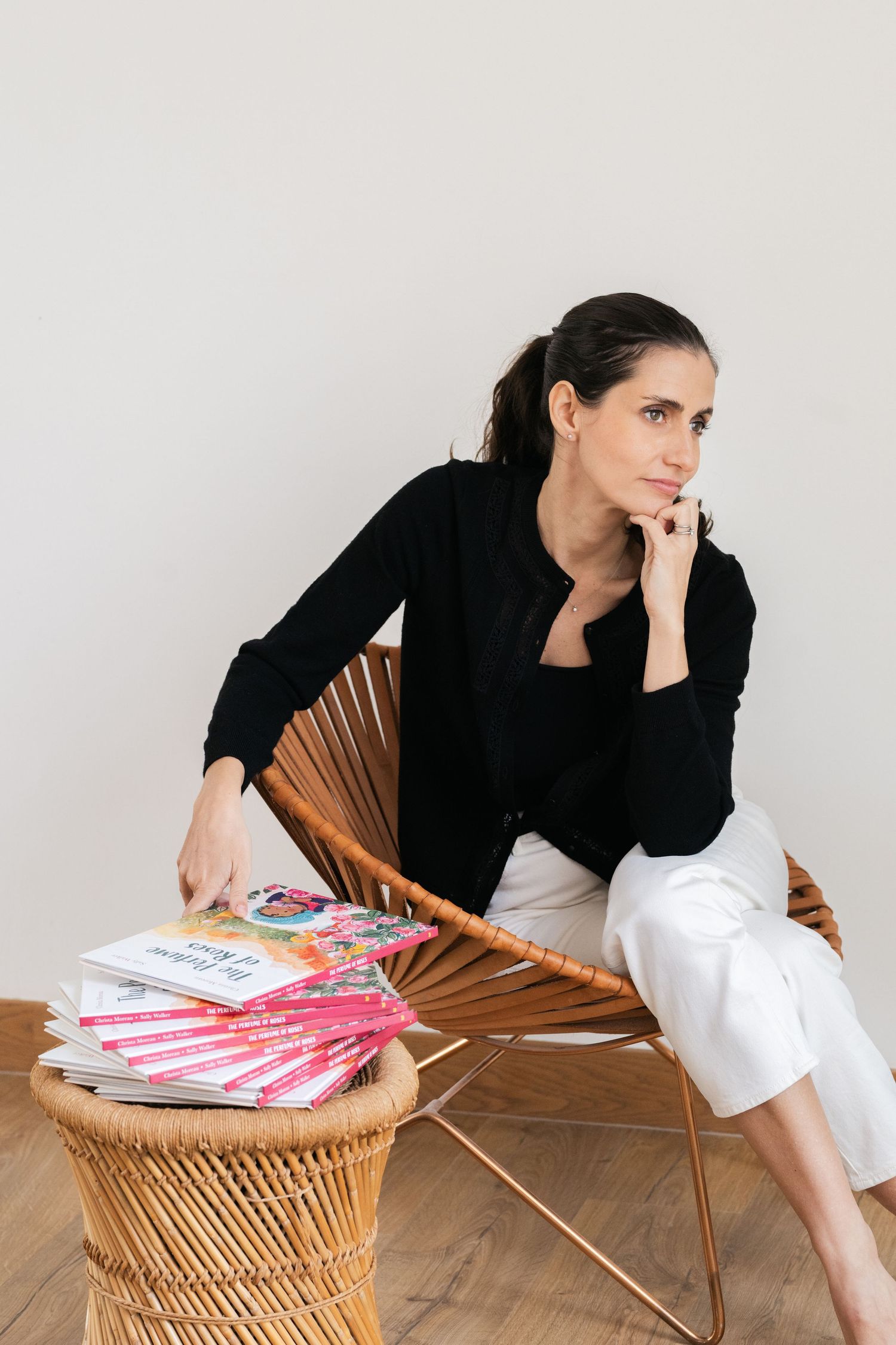 Relaxed pose in wicker chair with books and casual attire.