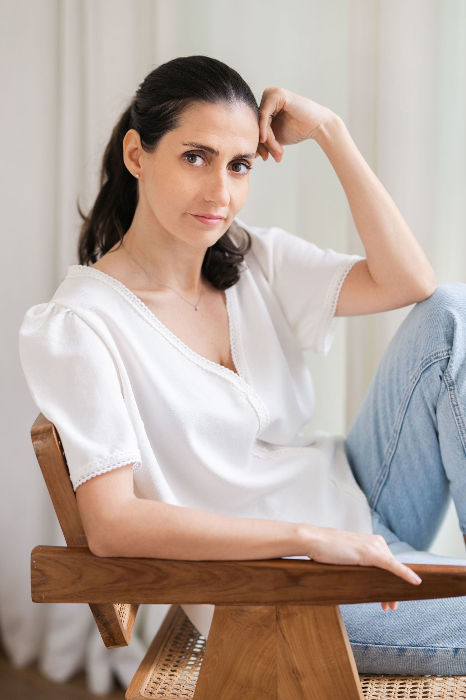 Woman in white top leaning on wooden table in minimalist setting.