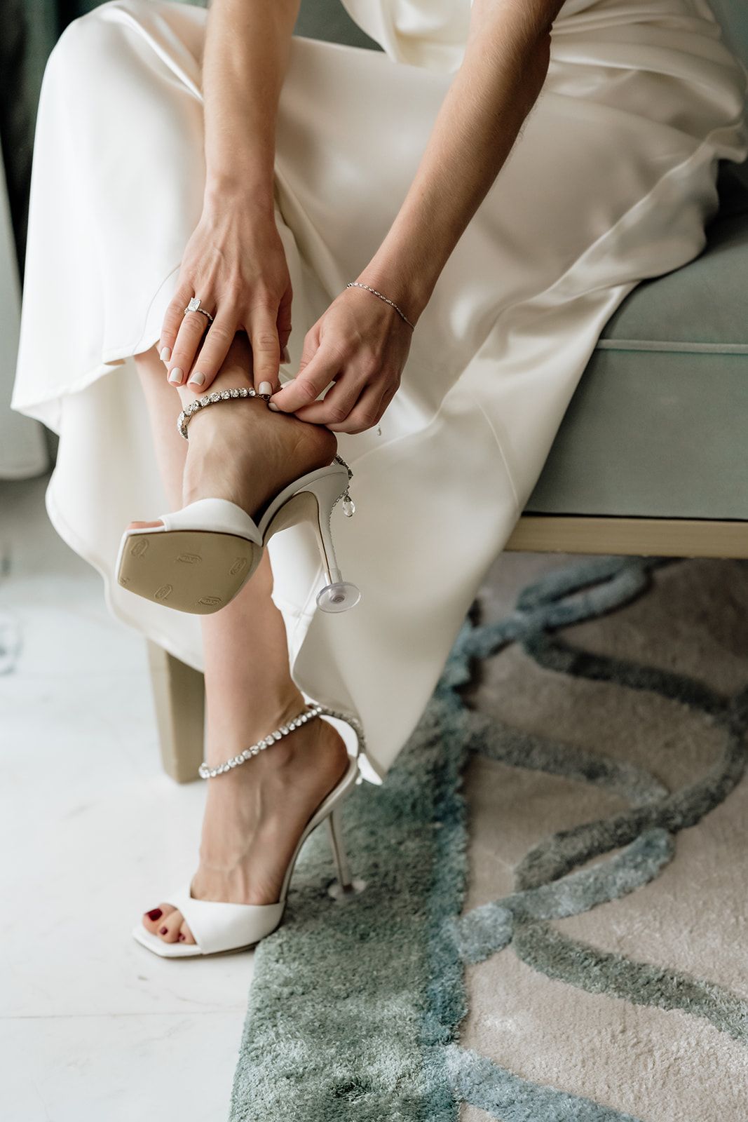 Close-up of white bridal shoes being put on with delicate pearl details and straps.