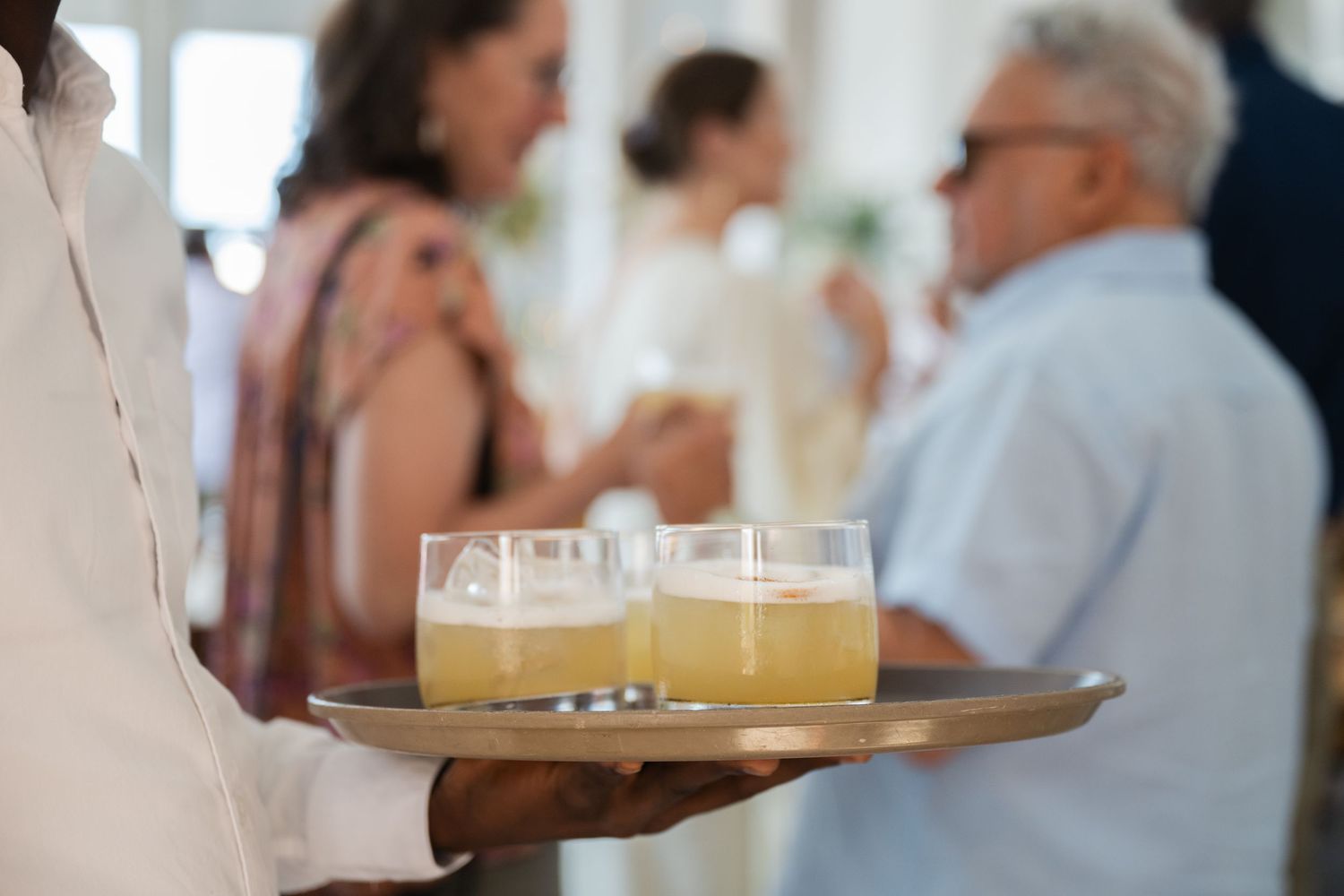 Server carries a tray of golden cocktails at an upscale event.