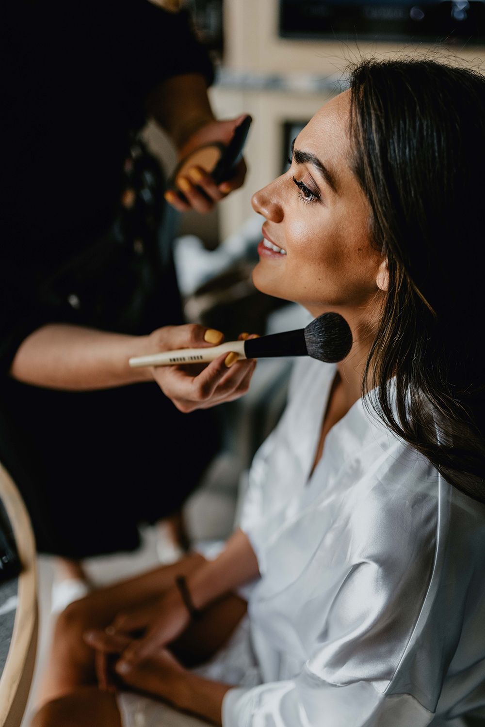 Makeup artist applying cosmetics with brush during bridal preparation.