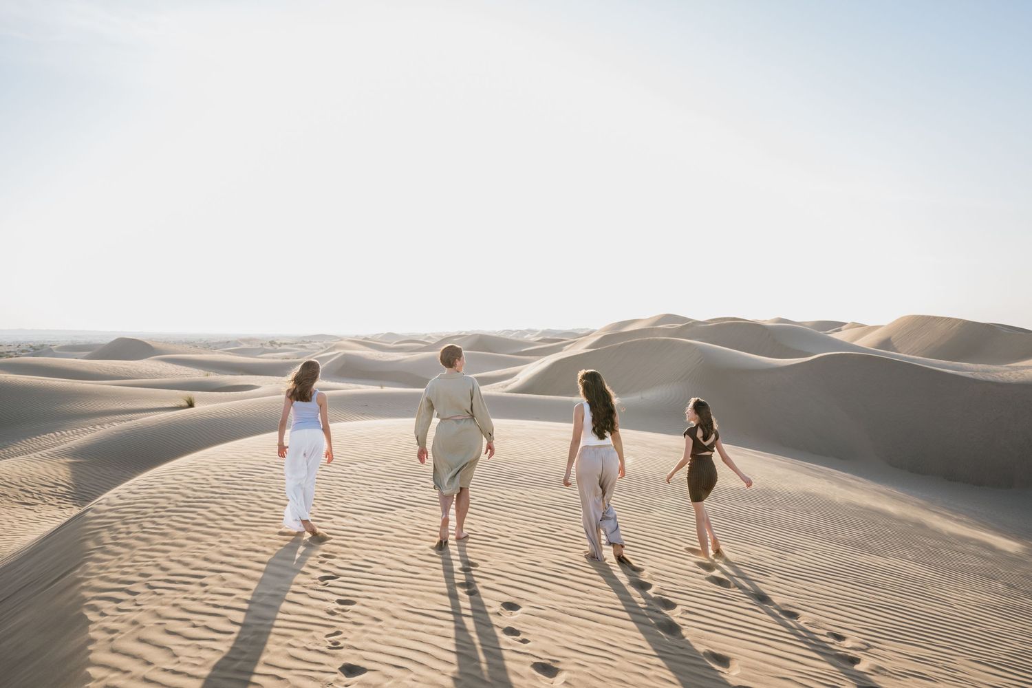 People walking along desert sand dunes under bright blue sky.