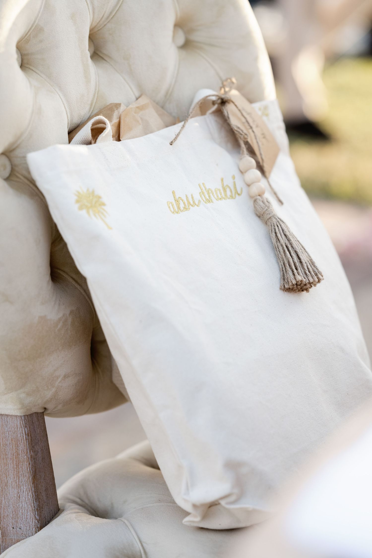 White decorative pillow with gold text and tassel detail resting on tufted chair.