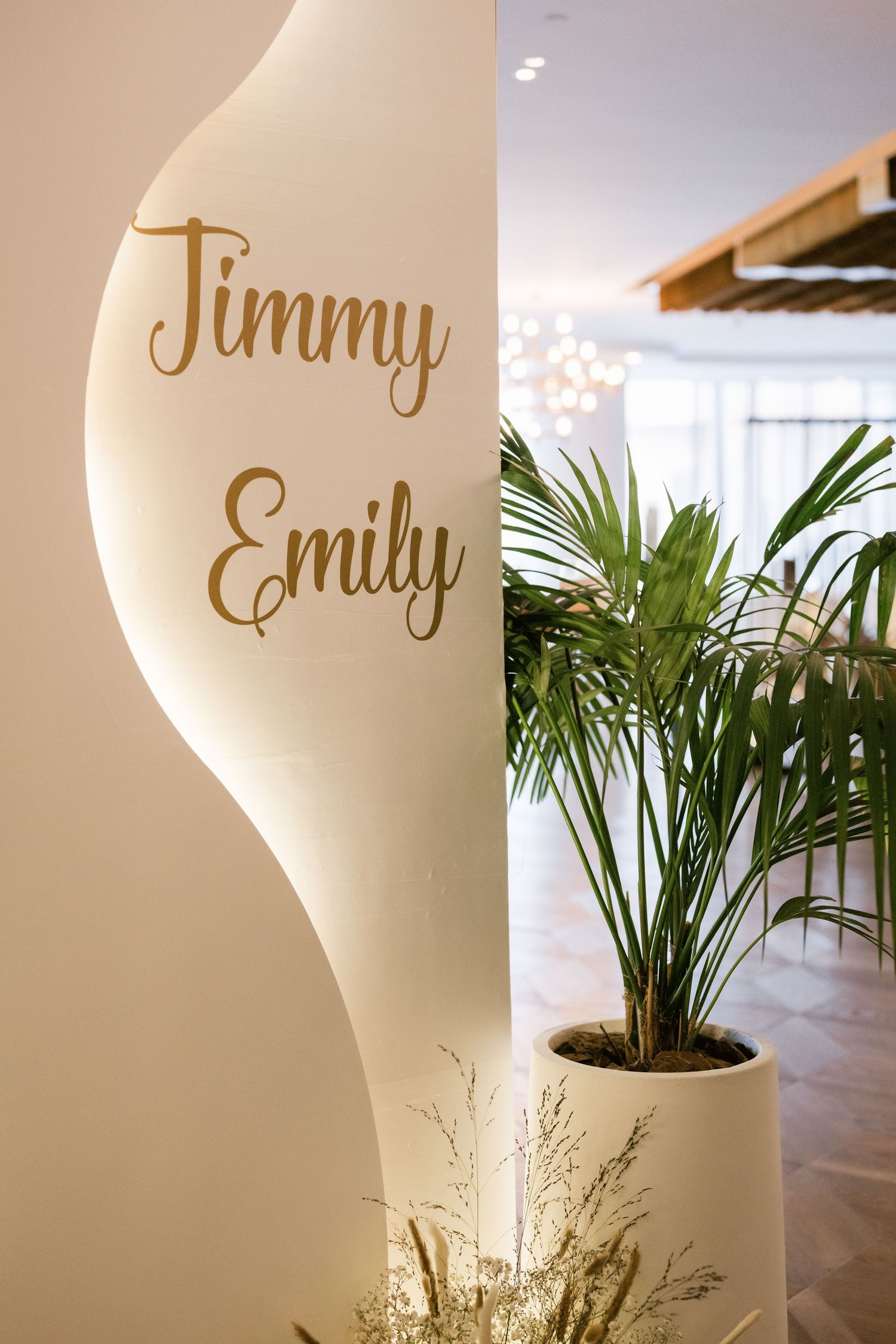 Decorative name signs with gold lettering against white curved wall with tropical plants.