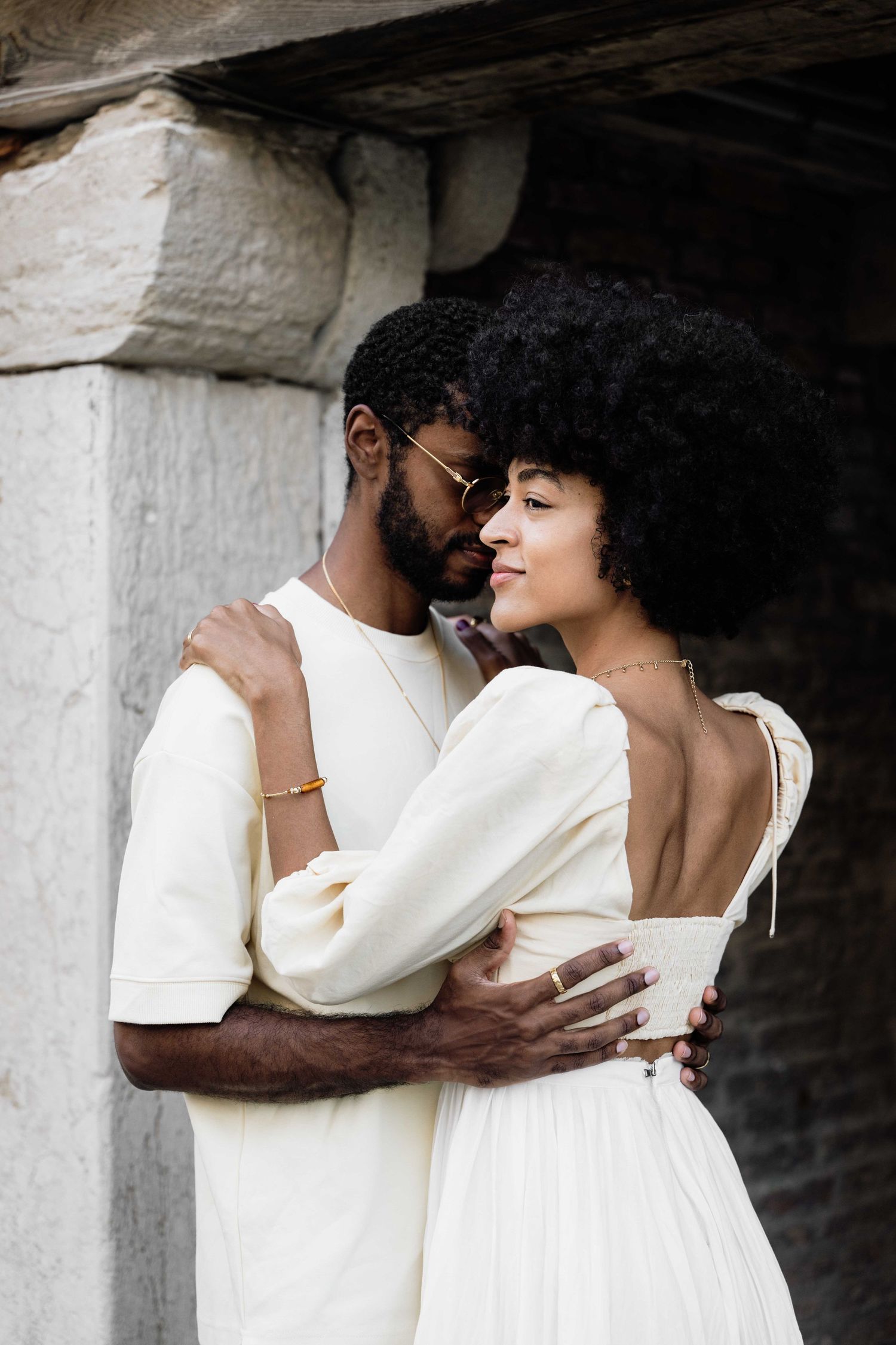 Intimate couple in white clothing embracing against stone columns.