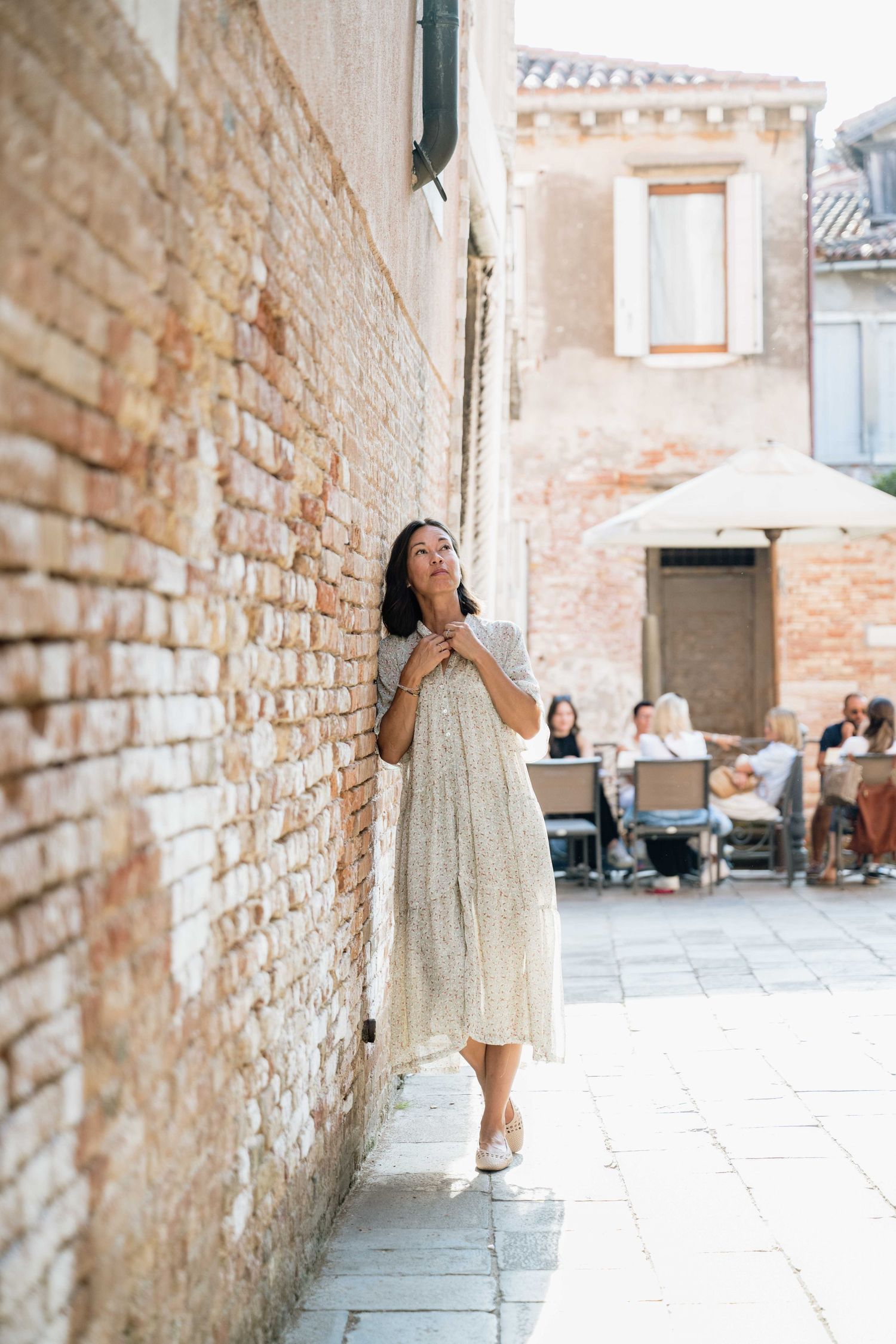 Person in flowy dress poses playfully against rustic brick wall in European alleyway.