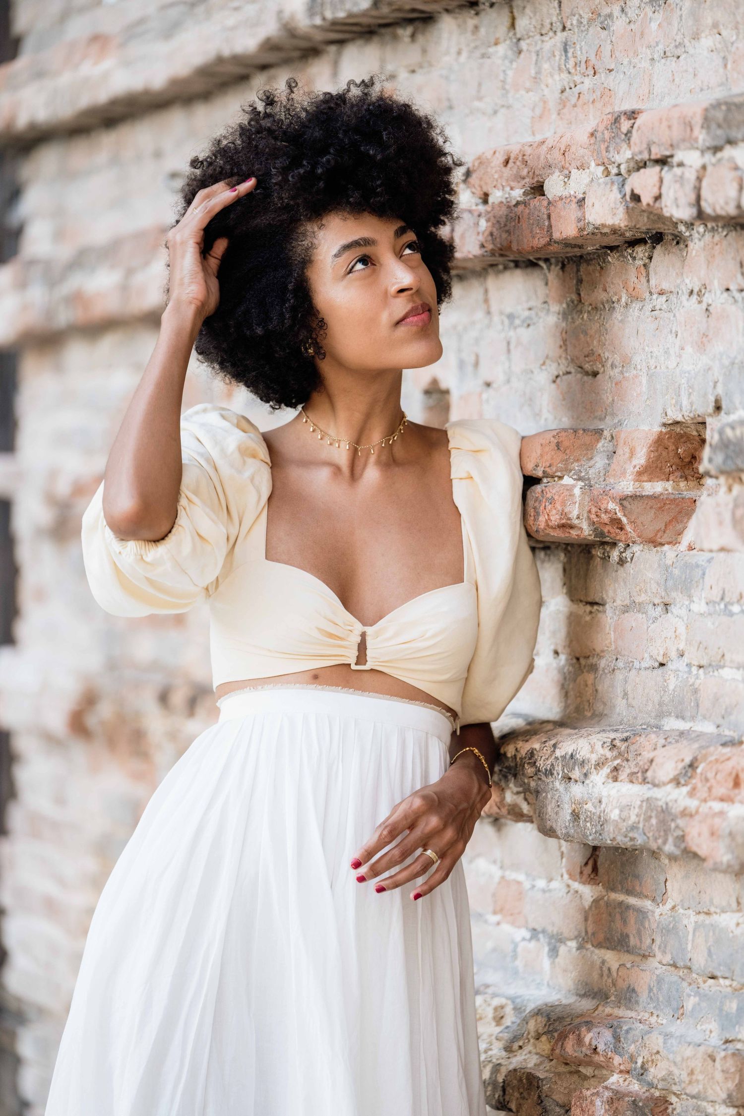 A romantic photoshoot featuring a couple in white outfits against a rustic brick wall.