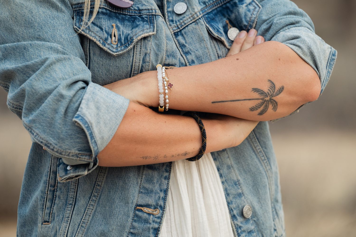 Close-up shot of a denim jacket sleeve with a small palm tree tattoo visible on the wearer's forearm.
